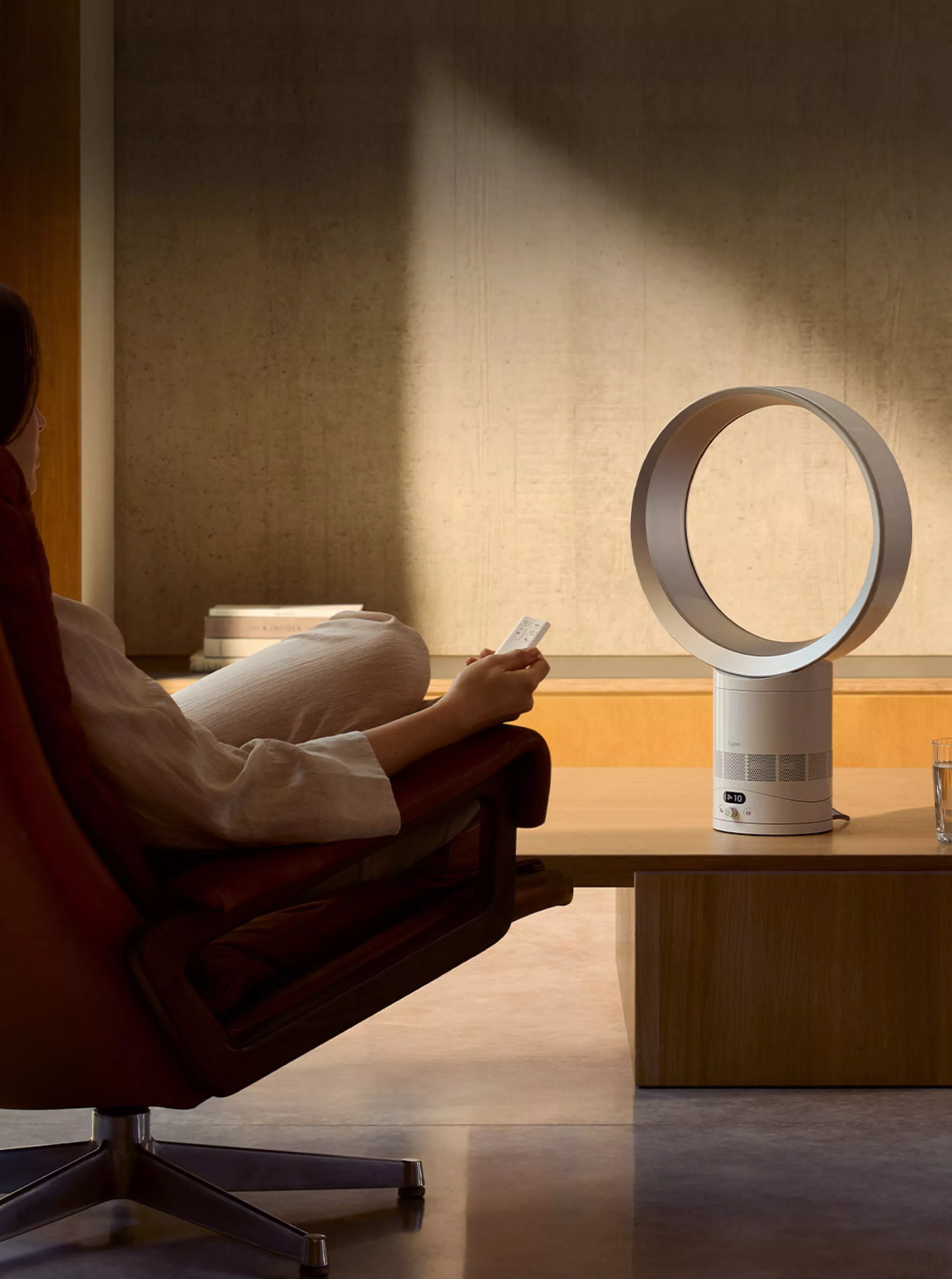 Person using remote to control a bladeless air purifier fan on coffee table in modern living room interior