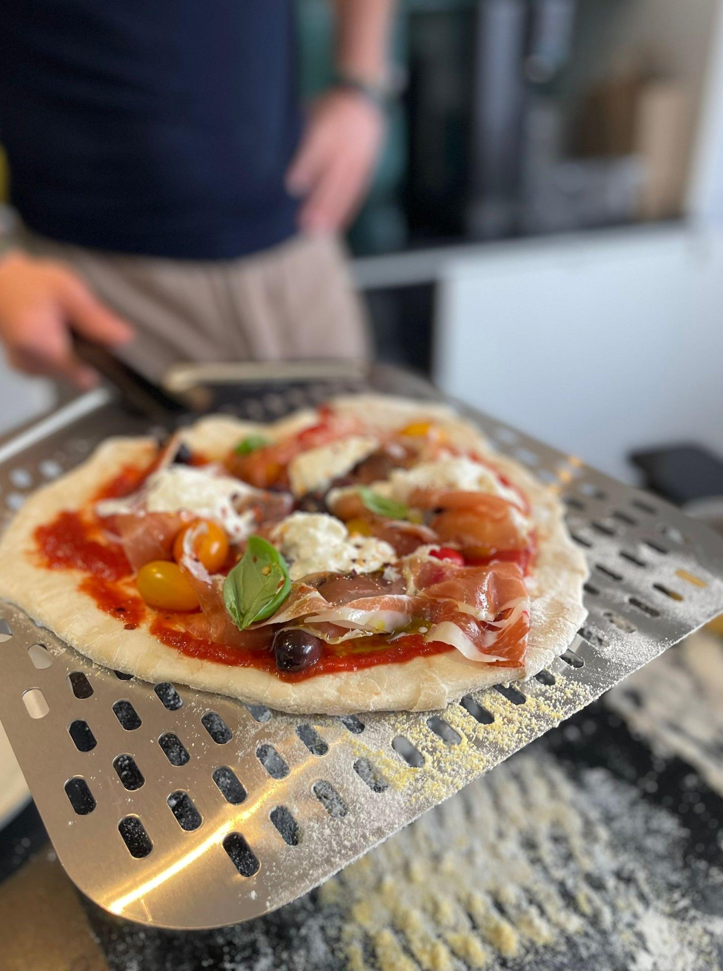 Pizza with various toppings on the pizza peel of the Ninja Artisan Electric Outdoor Pizza & Air Fry Oven