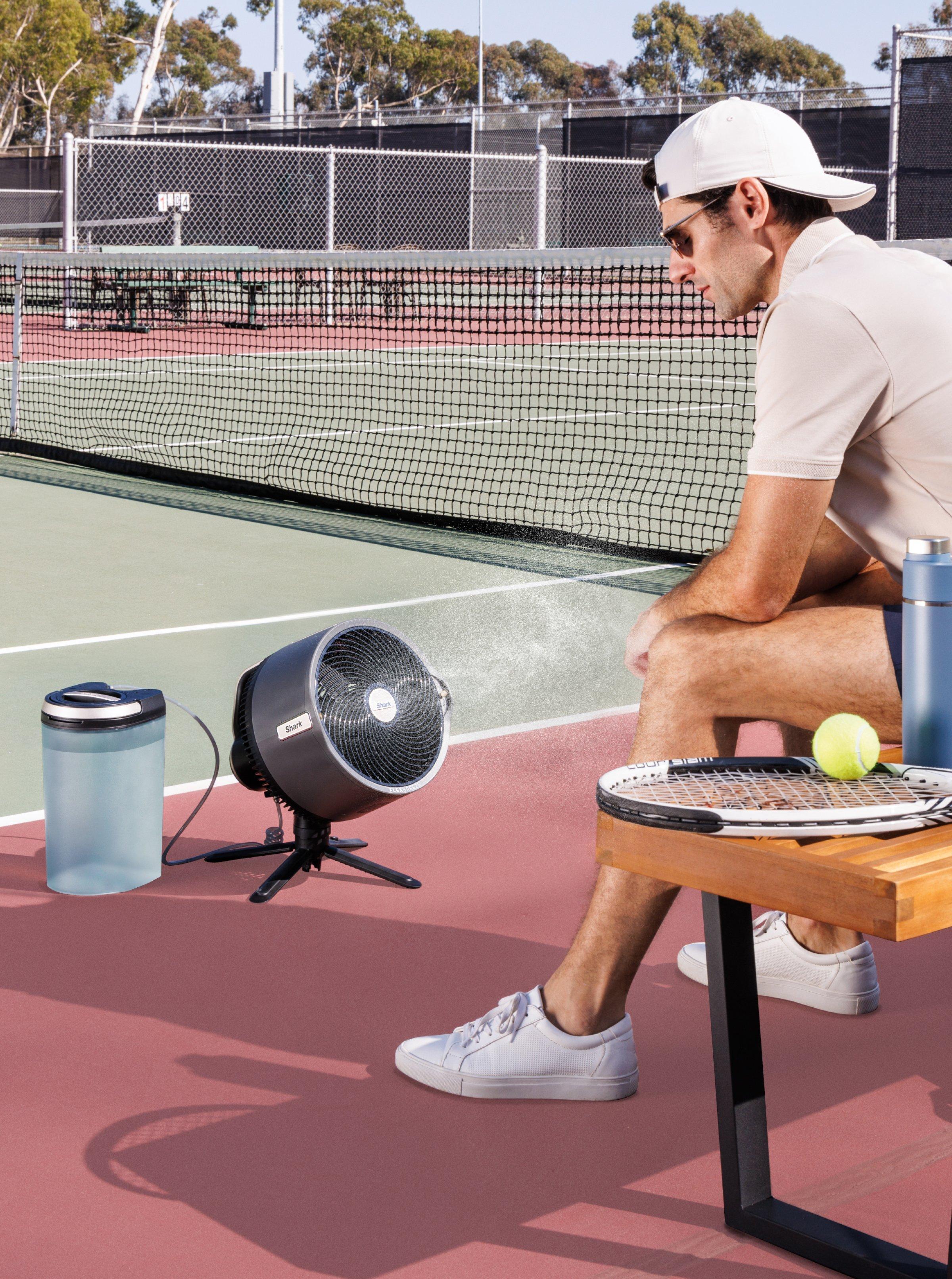 A male model sitting in front of the Shark FlexBreeze Pro Mist Fan on the tennis court