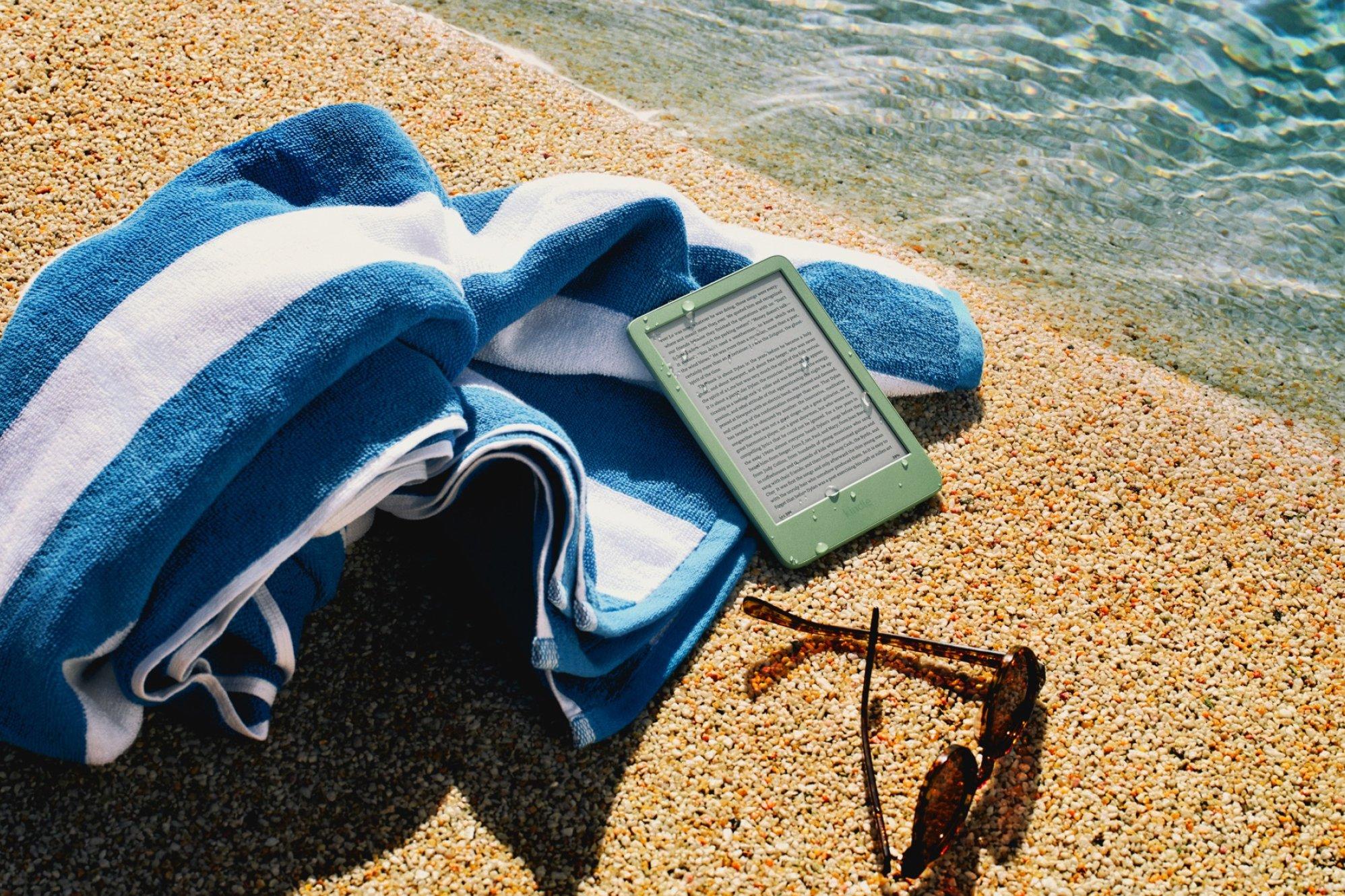 A large blue and white striped towel, a tablet, and a pair of sunglasses lying on the sandy beach