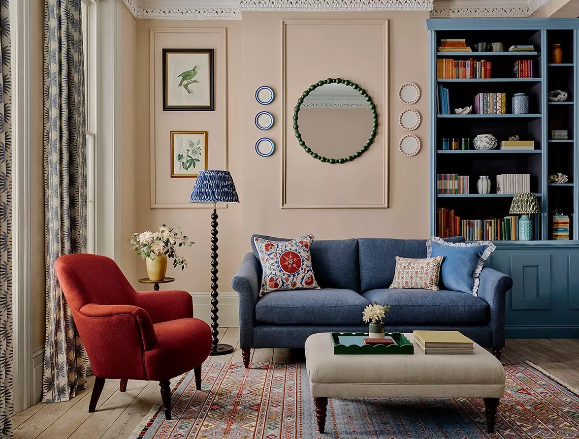 Stylish living room with blue sofa, red armchair, bookcase, patterned rug, and decorative wall art and mirror.