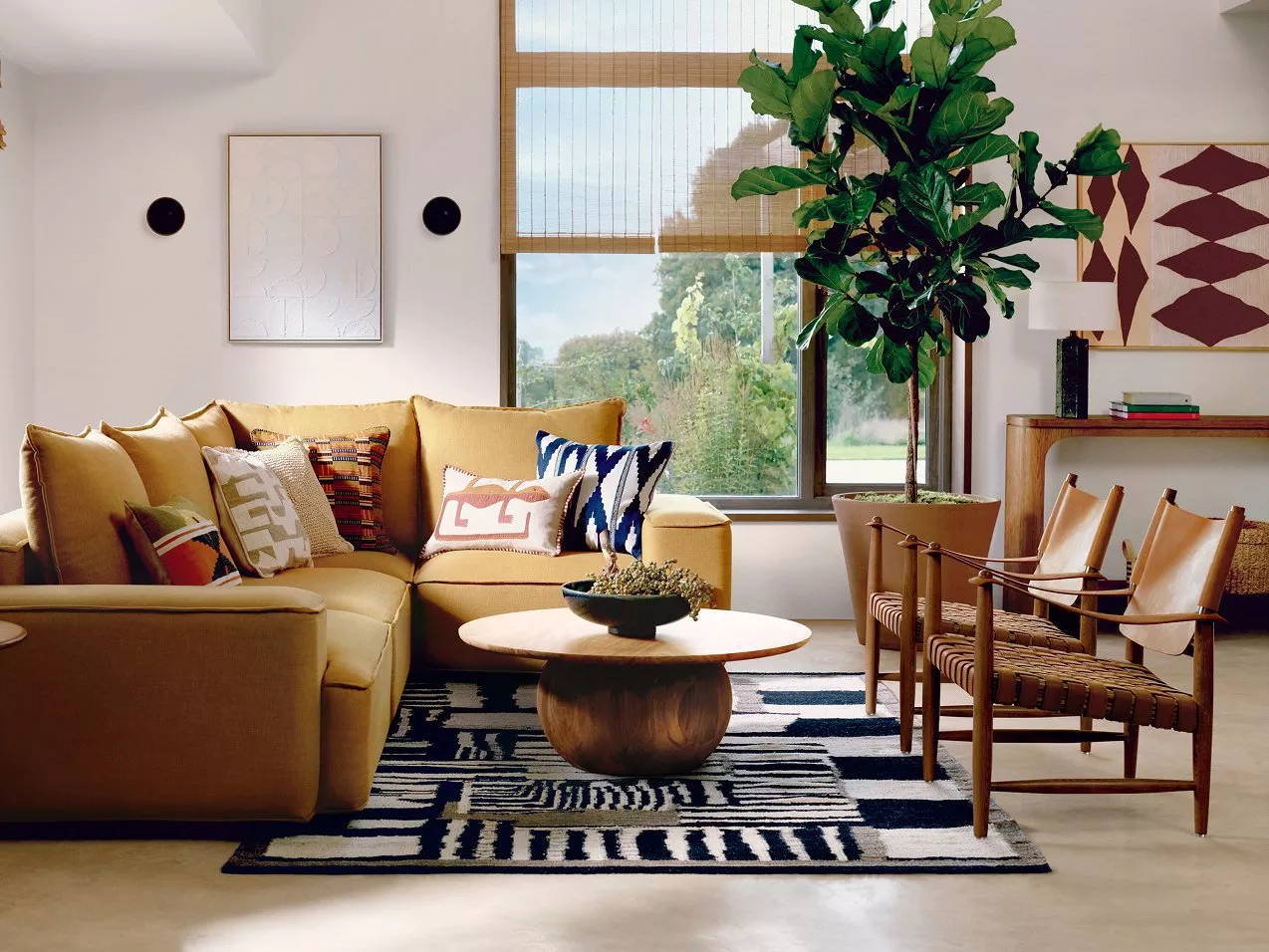Living room with a mustard sofa, patterned cushions, wooden chairs, and large windows.