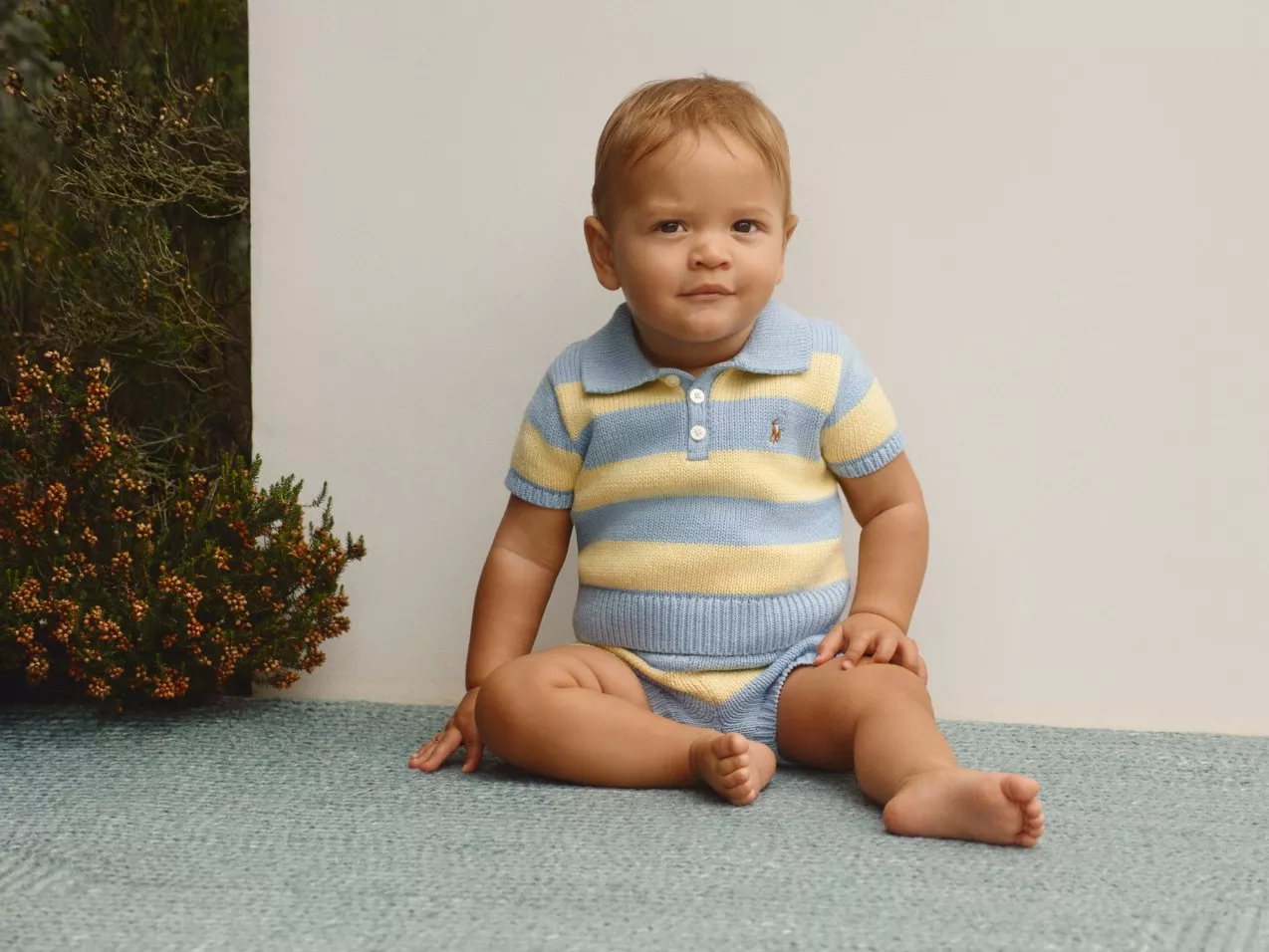 Baby with a stripe yellow and blue collared short sleeved sweater and shorts.