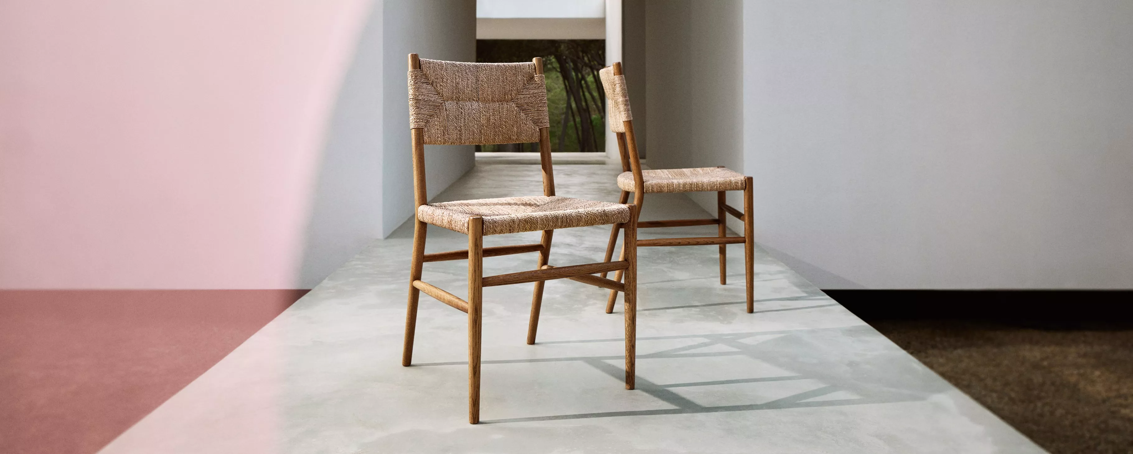 Two wooden chairs with woven seats and backs, against a concrete backdrop