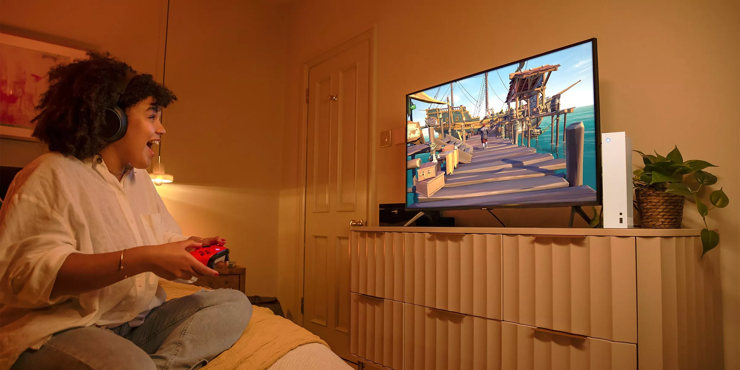 Gamer wearing headphones plays Xbox Series S with controller, watching an adventure game on a TV in bedroom.