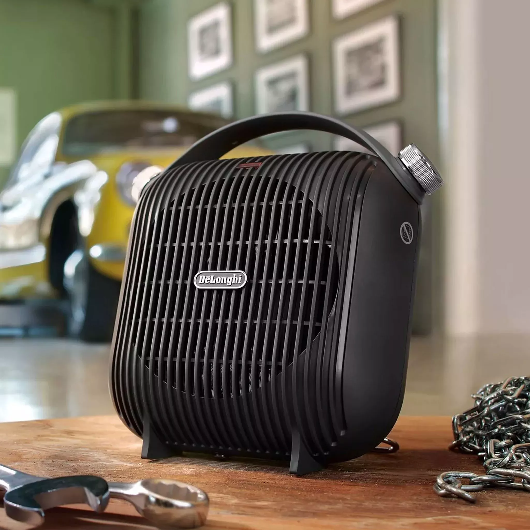 De’Longhi portable fan heater on a workbench in a garage, with blurred classic car and tools in background