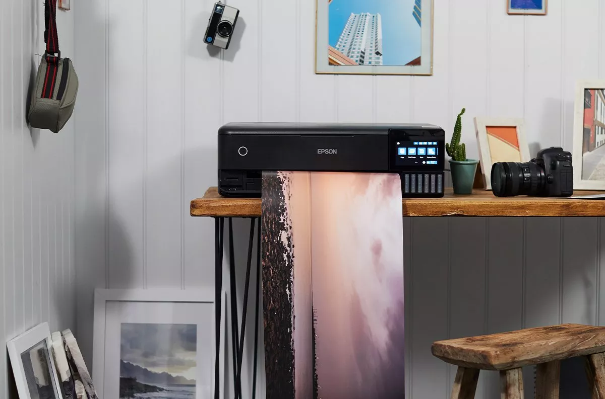 Epson photo printer on wooden desk printing large fine art photograph, home studio setup with camera and frames