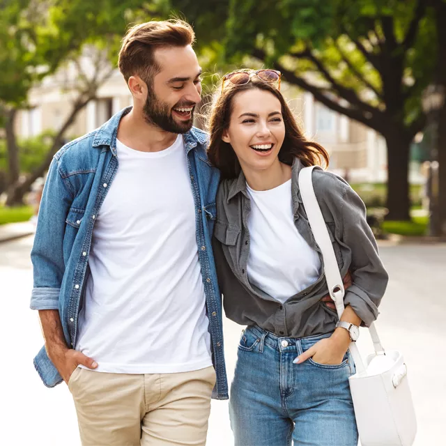 Smiling young couple walking outdoors in a leafy park, casual denim outfits, relaxed summer lifestyle moment