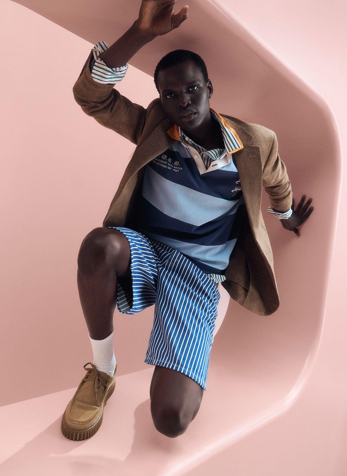 A man wearing chino shorts, rugby top with a brown suit jacket