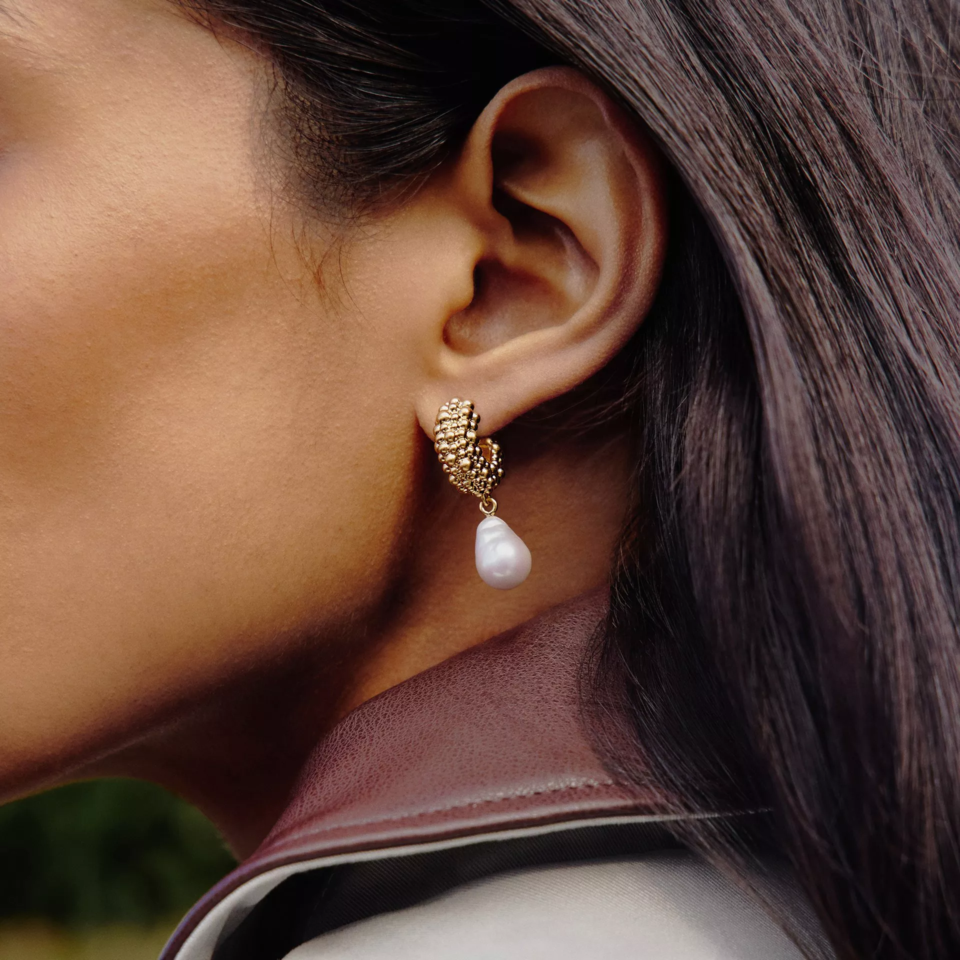 Close-up of woman's ear wearing a gold hoop earring with dangling white pearl, luxury jewellery detail shot