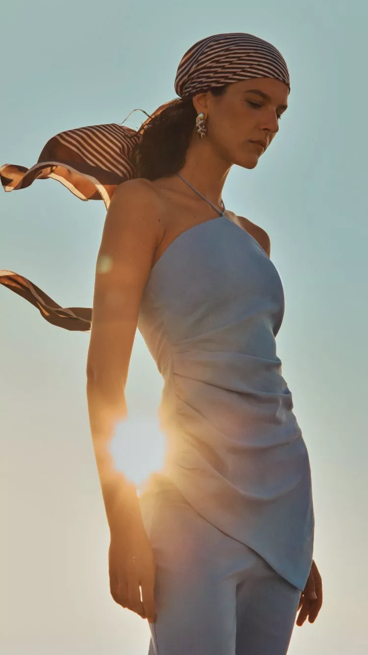 Fashion model in pale blue dress with striped headscarf, photographed outdoors at golden hour with sun flare