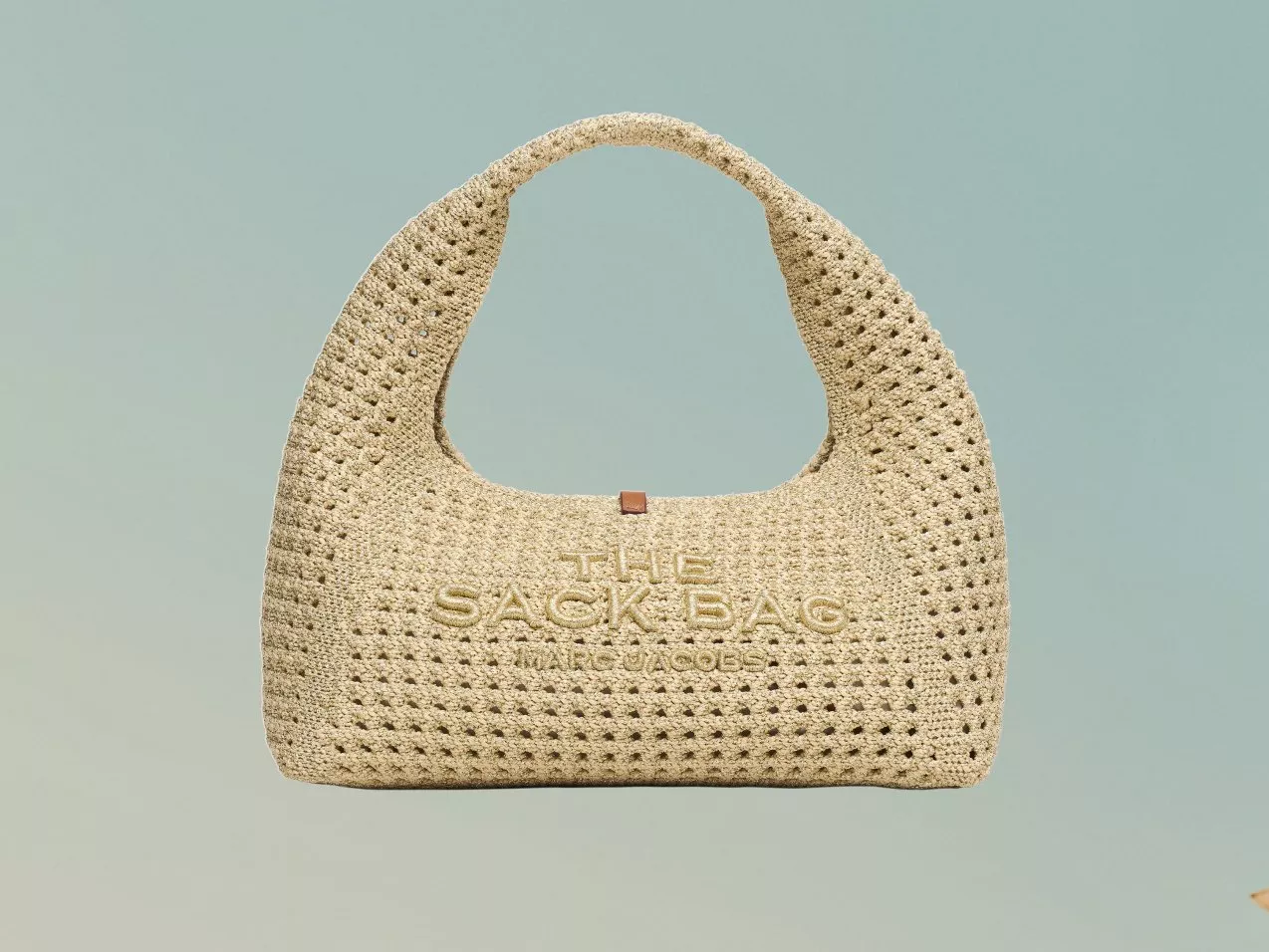 Beige woven raffia hobo bag with cut-out crochet detailing and embossed logo, studio product photo on grey backdrop