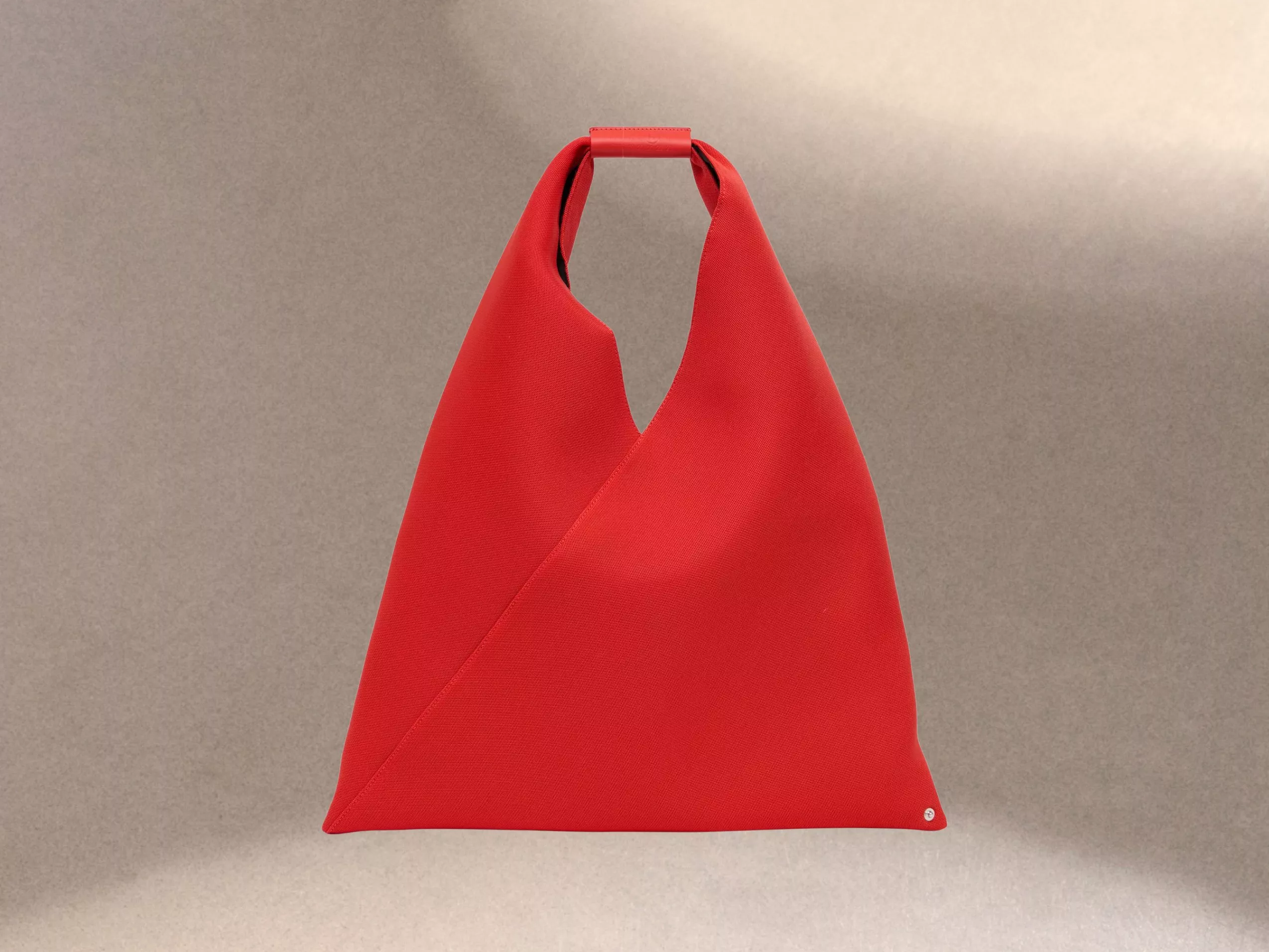 A vibrant red, triangular handbag with a minimalist design, featuring a unique folded top handle.