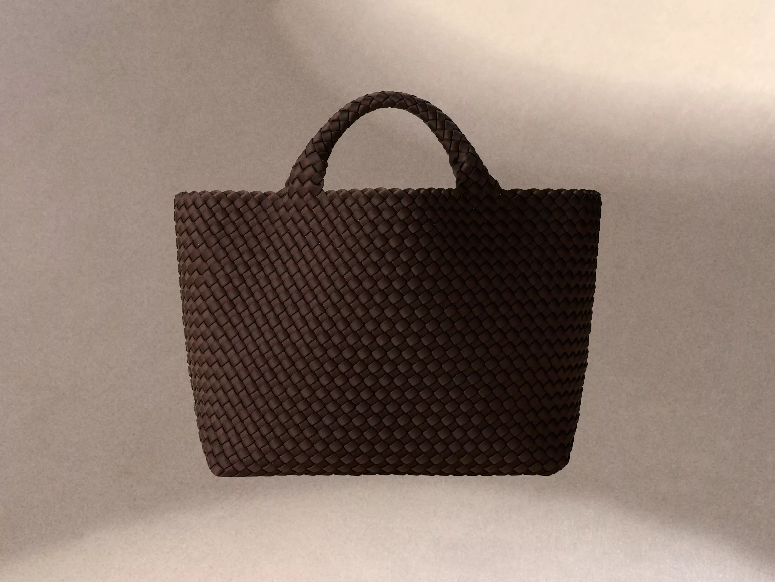A woven brown handbag with a textured surface and sturdy handle, set against a soft, neutral background.