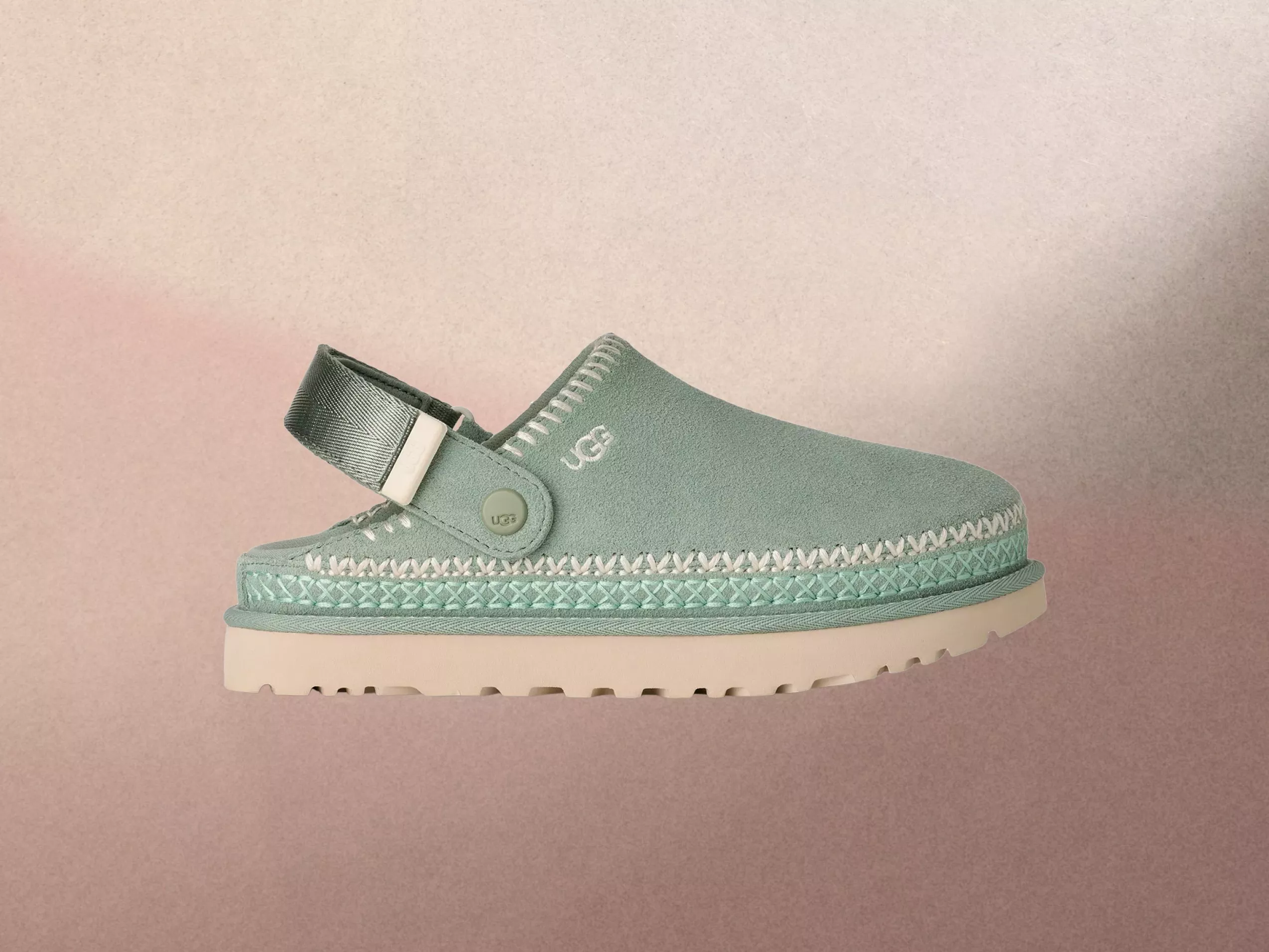 Side view of a green suede clog with a strap, featuring UGG branding, on a textured beige background.