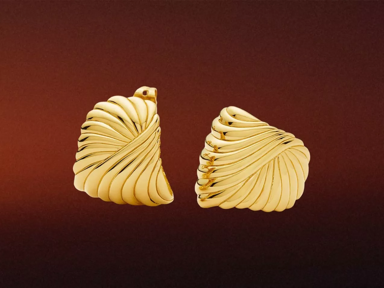 Pair of sculpted gold statement earrings with spiral ridged design, photographed on a warm brown background