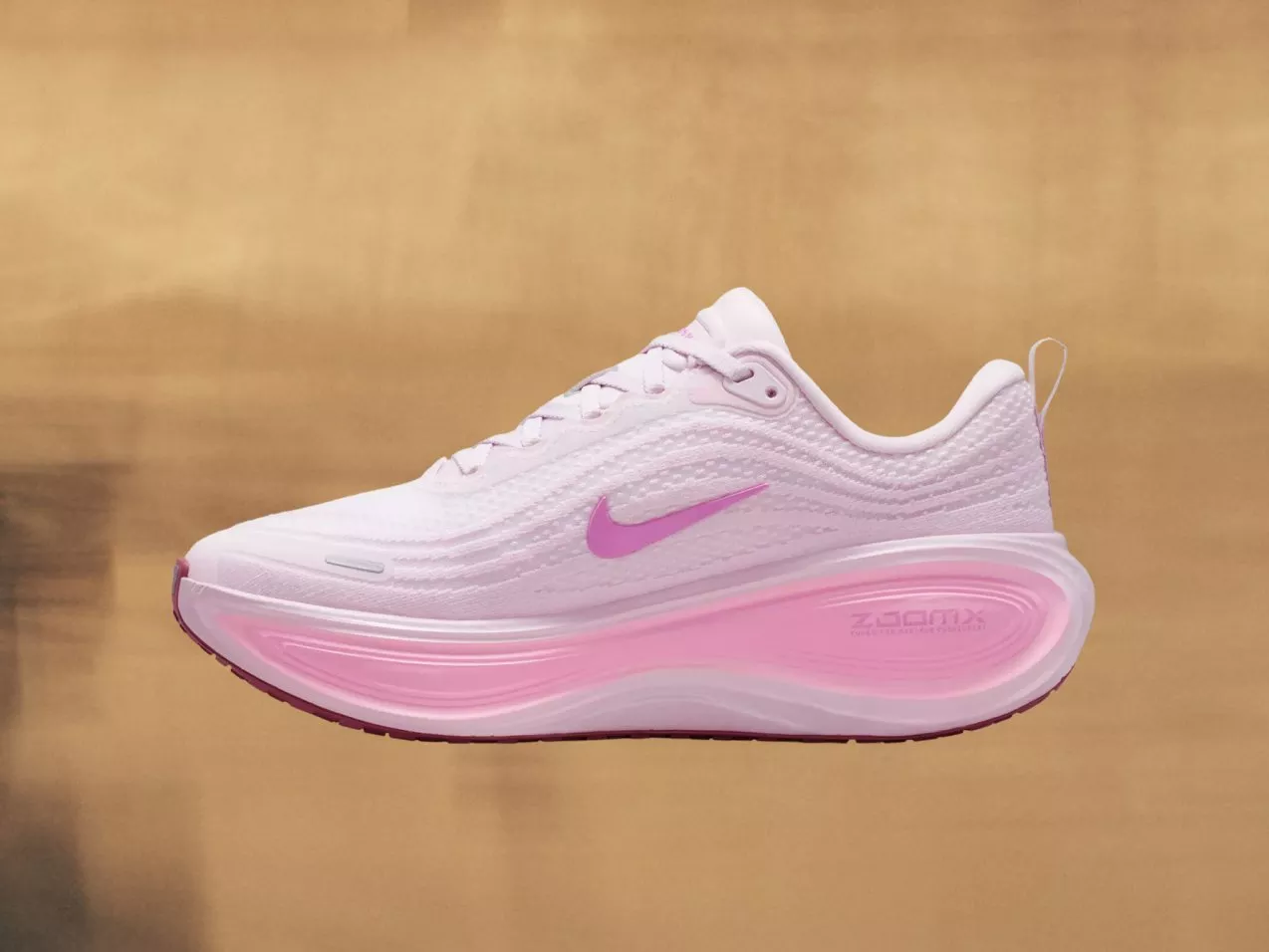 Side view of pale pink Nike running trainer with ZoomX cushioned sole, on neutral beige background