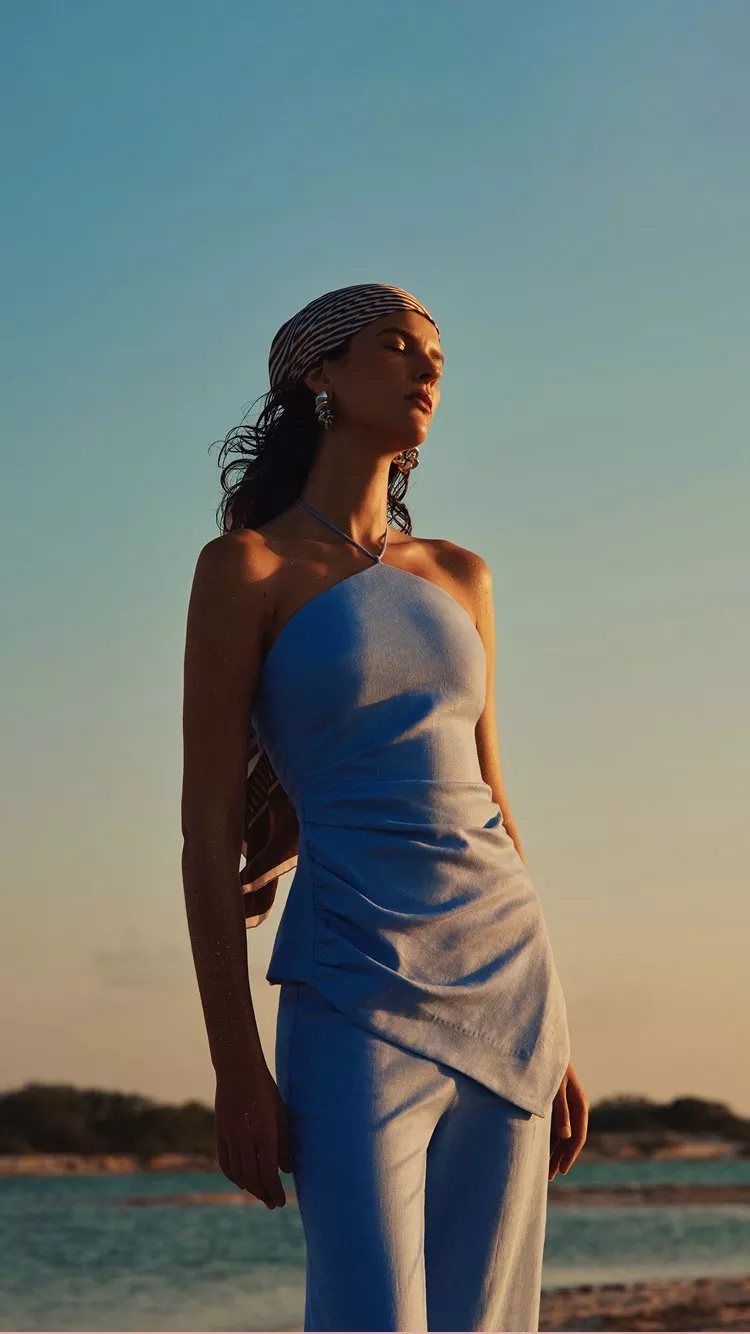 Woman in a blue summer top and headscarf standing outdoors at sunset under a clear sky