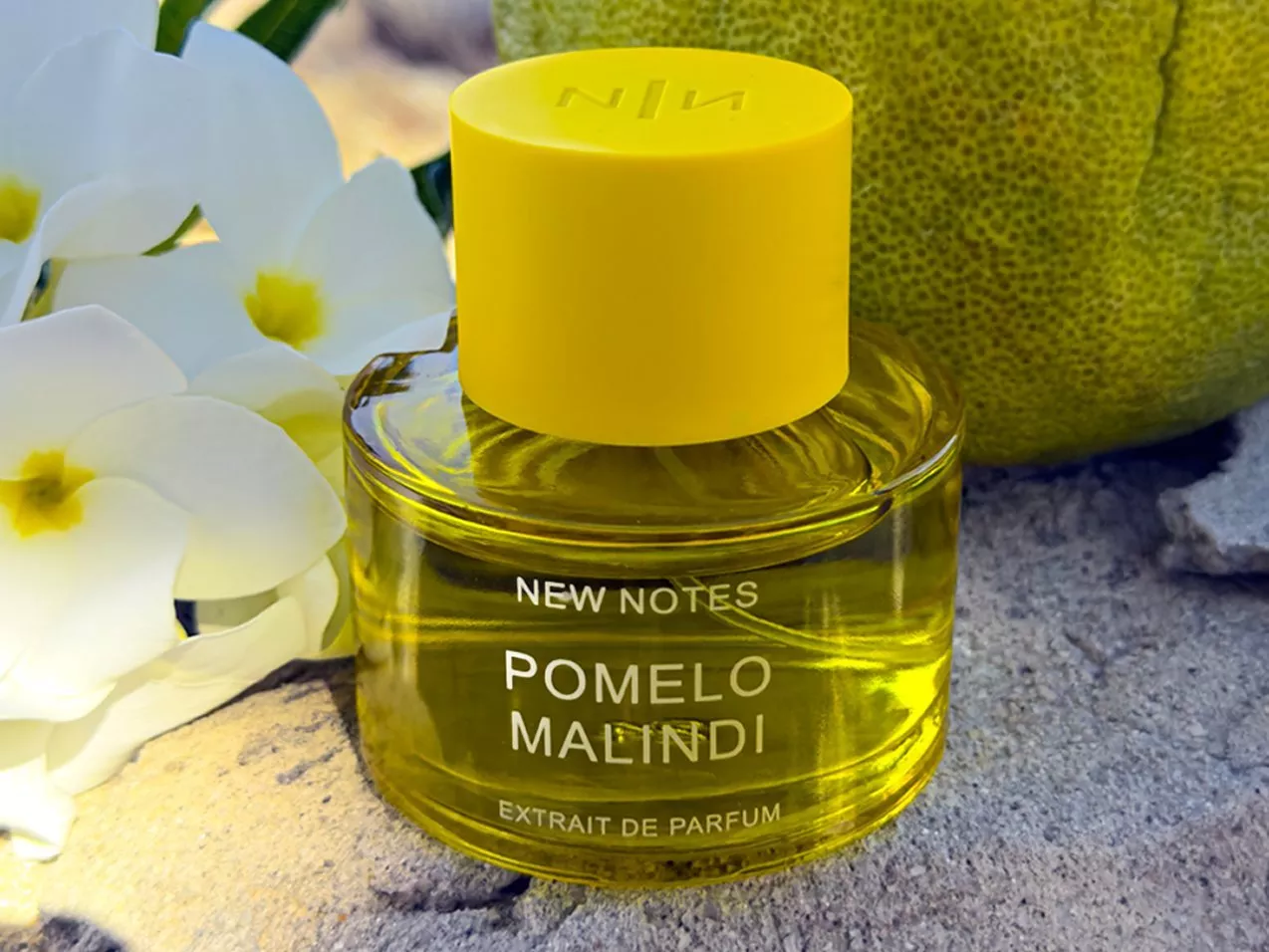 New Notes Pomelo Malindi extrait de parfum bottle with yellow cap, beside white flowers and pomelo fruit