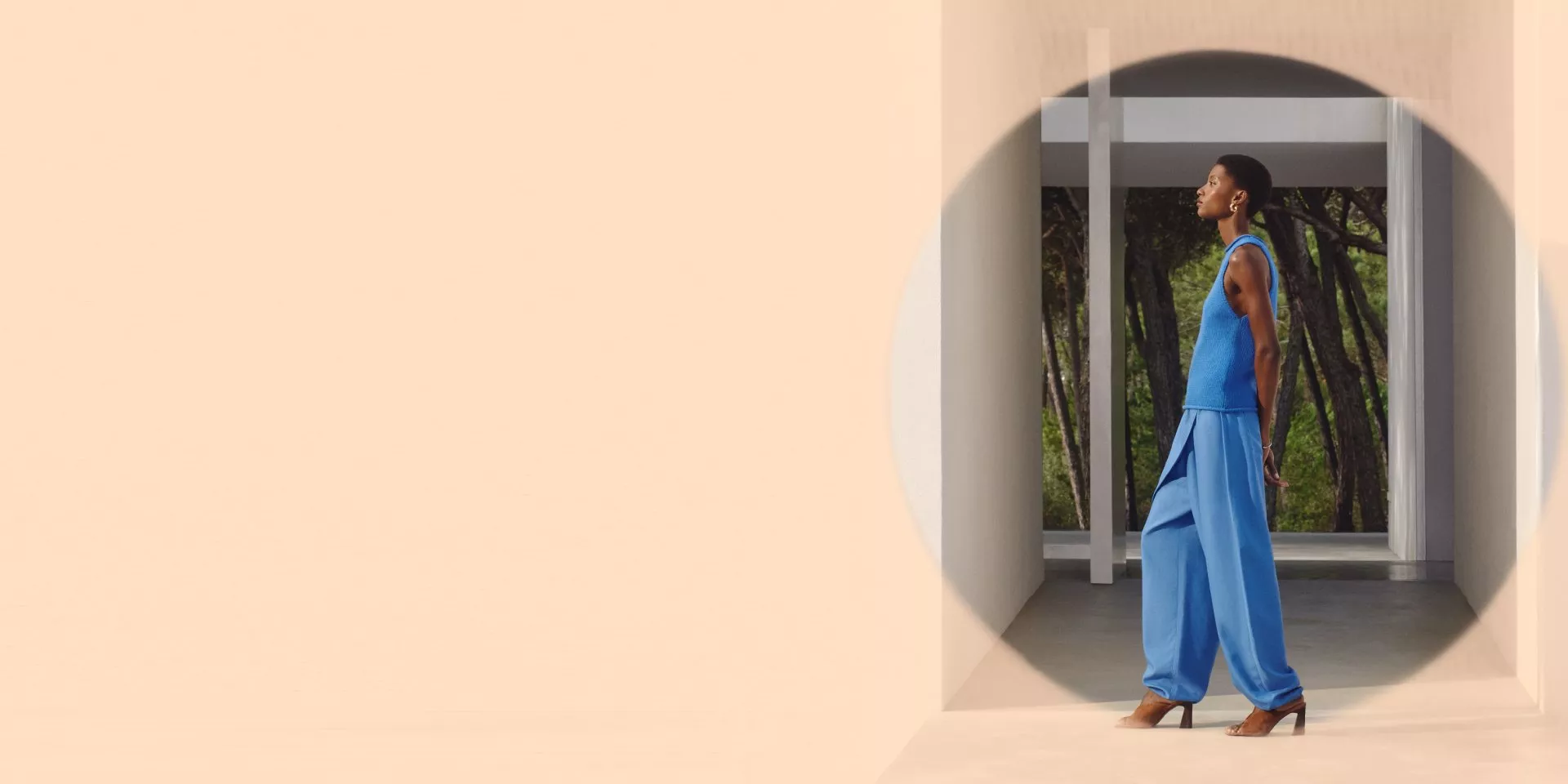 A person walks confidently in a stylish blue outfit and heels, set against a modern architectural backdrop.