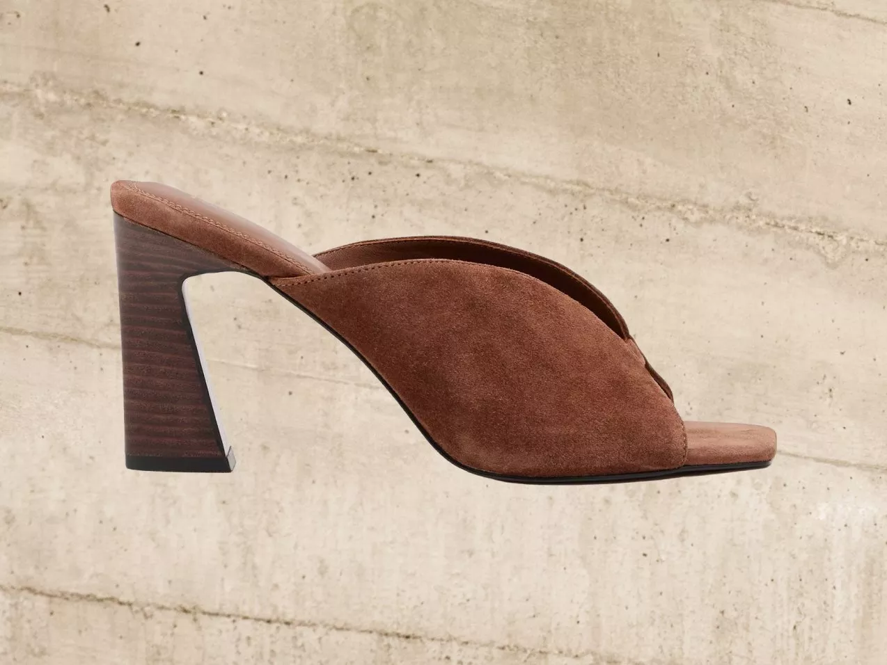 Brown suede high heel mule against a textured concrete background, showcasing elegant fashion footwear design.