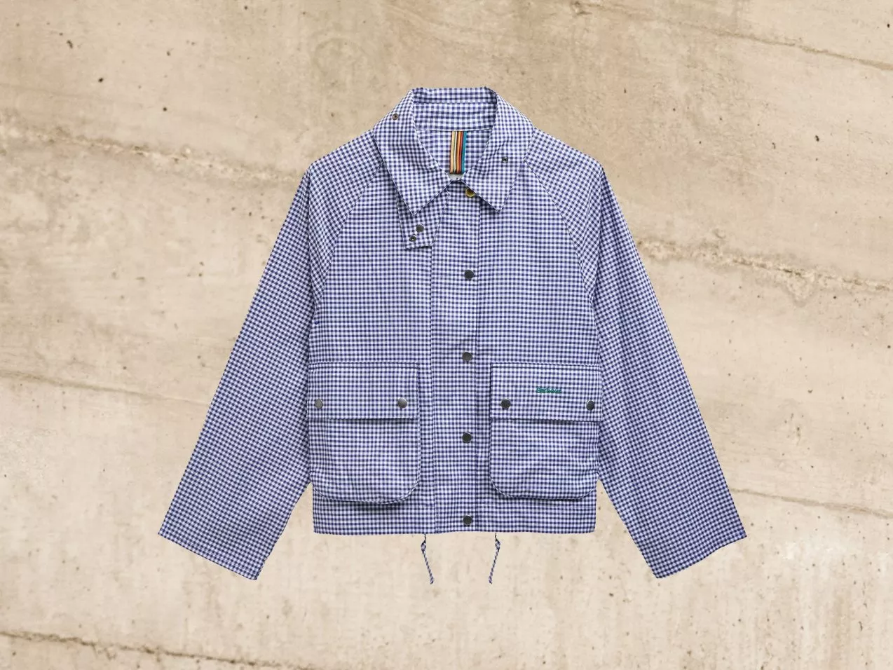 Blue and white checkered jacket with front pockets and a collar, set against a textured beige background.