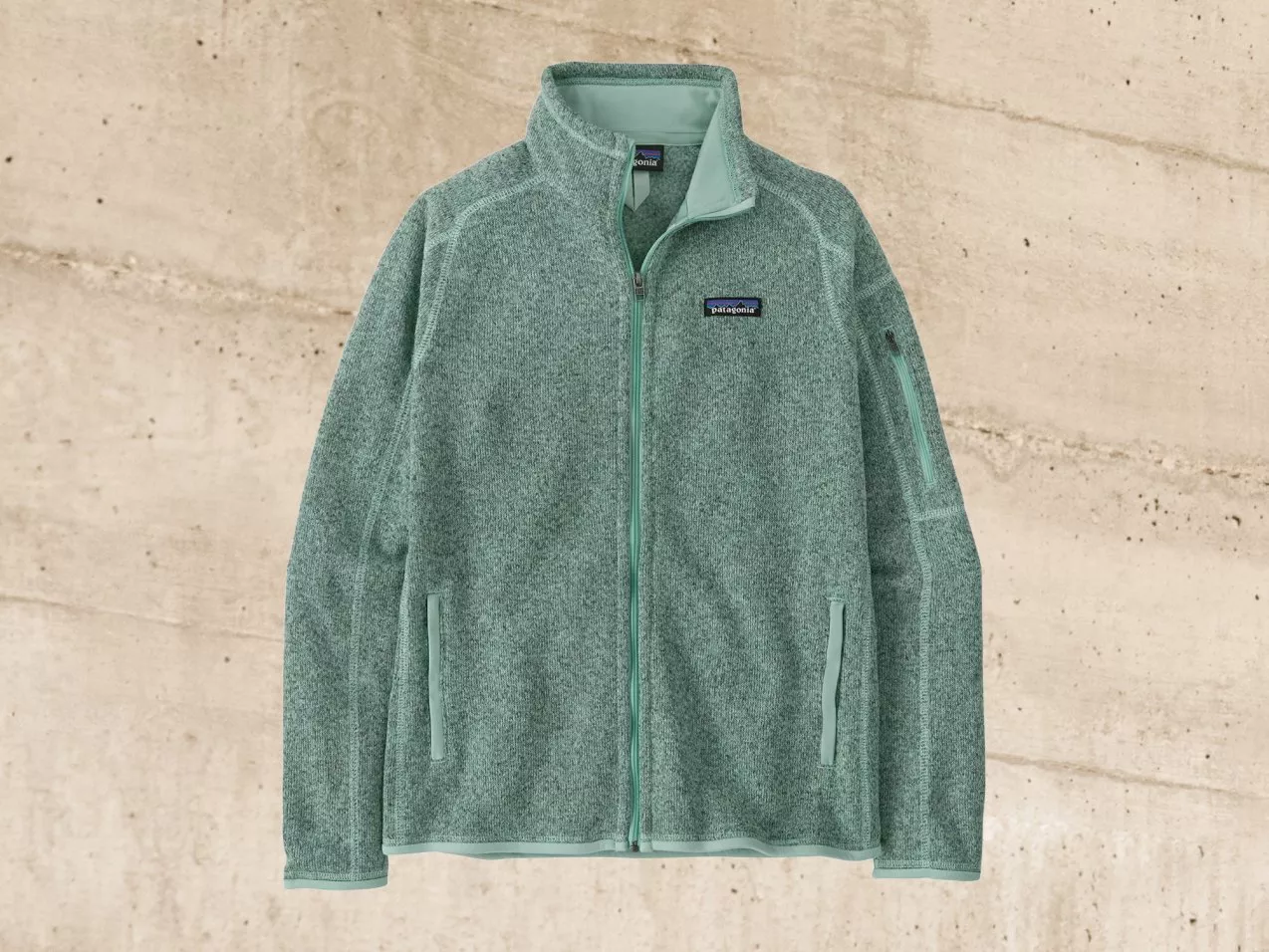 Light green fleece jacket with zip front and pockets, displayed against a textured beige background.