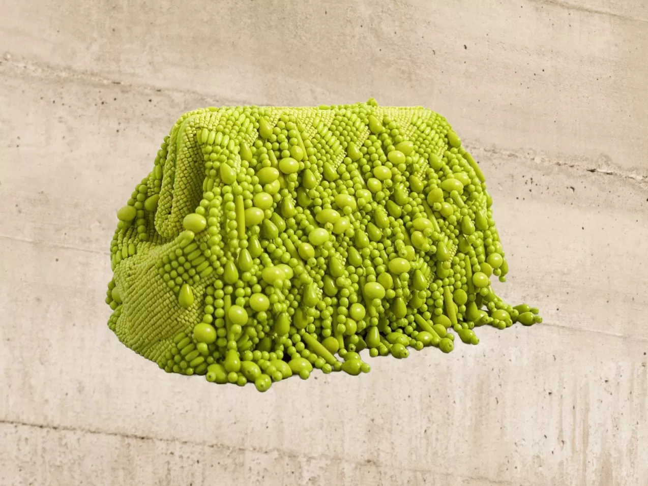 A green textured bag with bead-like embellishments against a concrete background, creating a striking contrast.