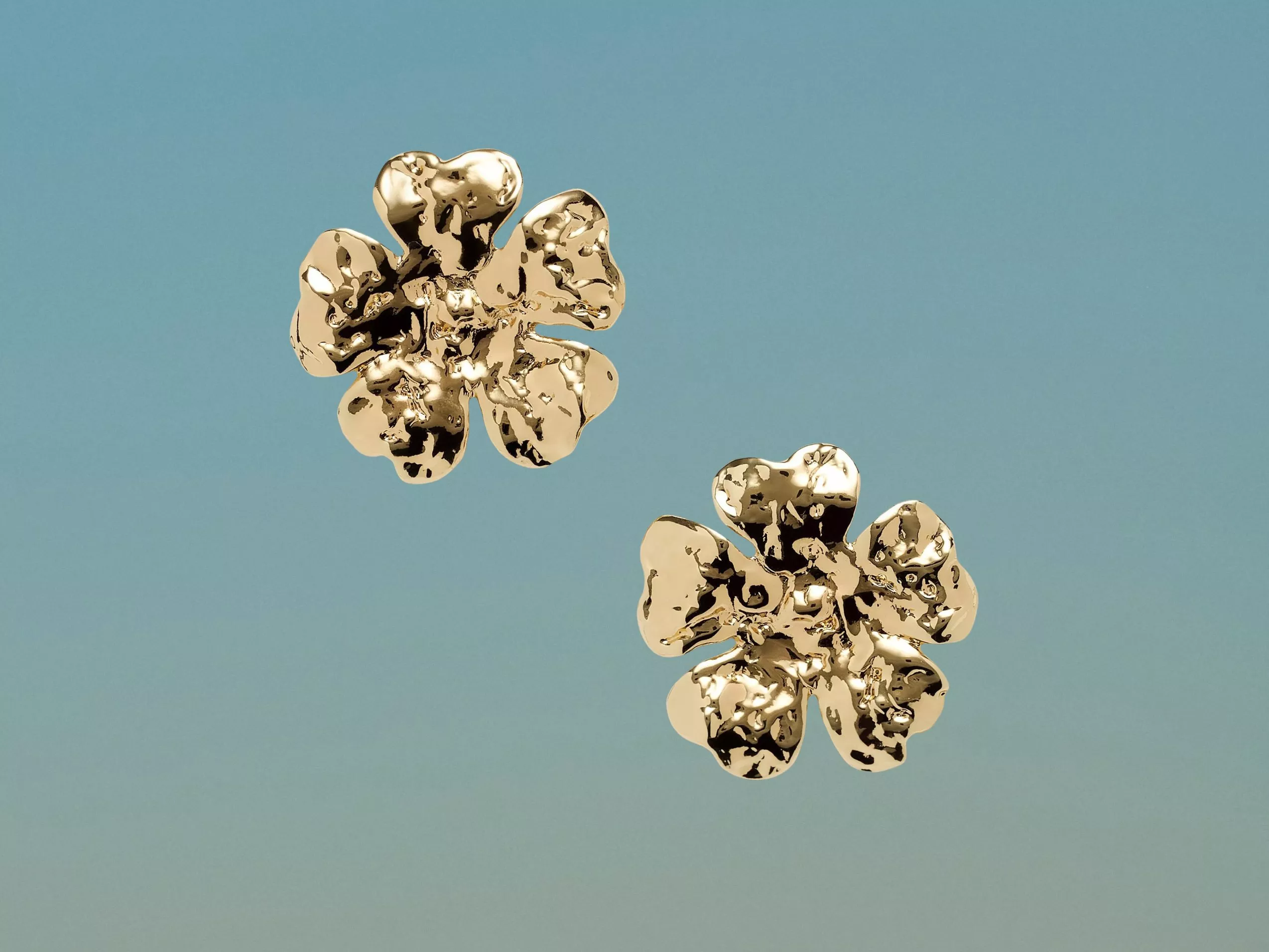 Pair of shiny gold flower-shaped stud earrings on a light blue background