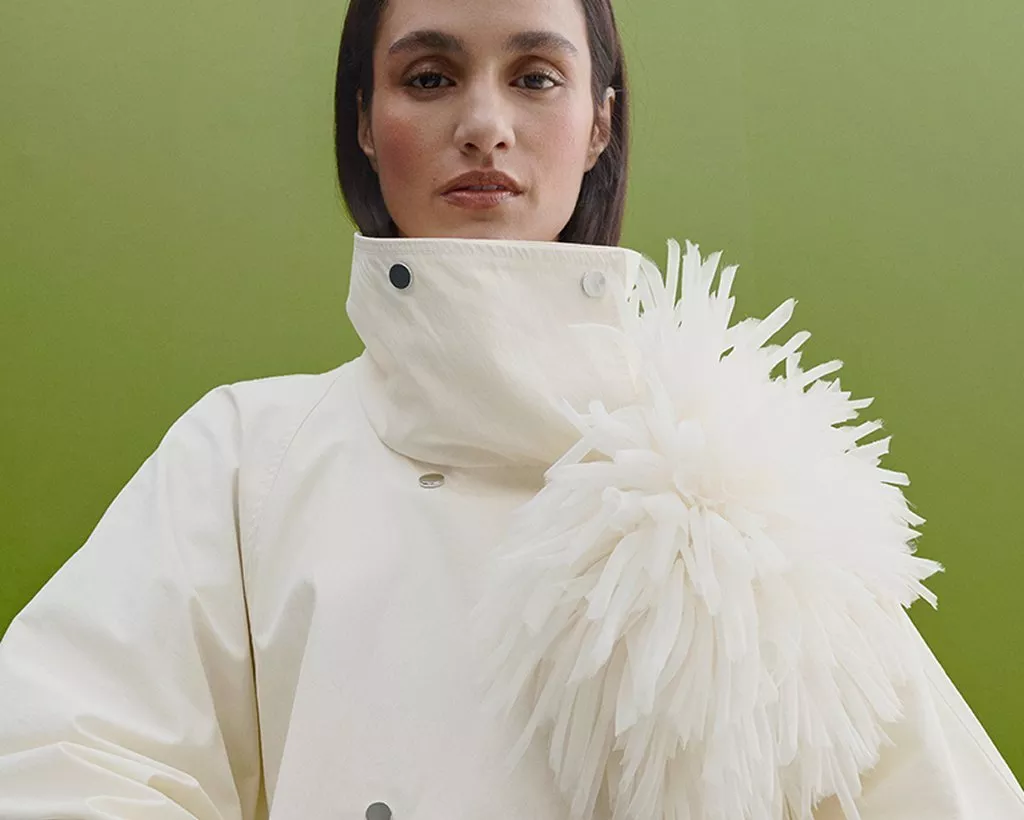 Fashion portrait of woman in white high-collar coat with feather detail, against green studio backdrop
