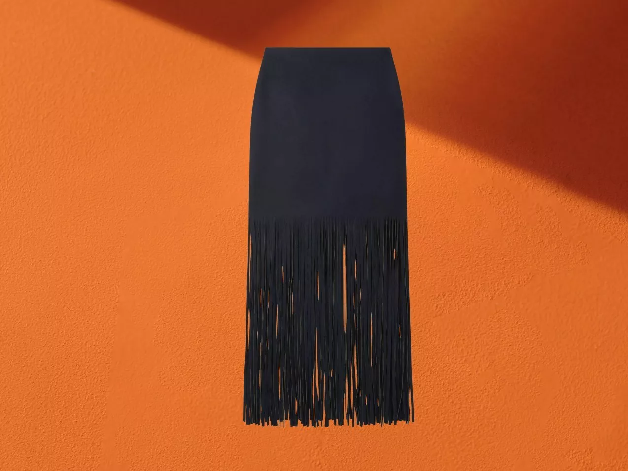 Black fringe midi skirt on orange background, minimalist fashion product photo with strong shadow and texture