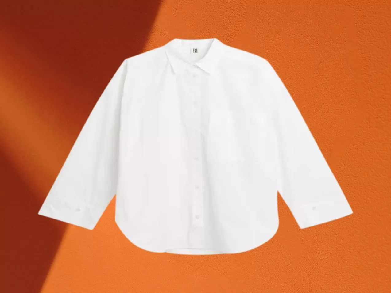White long-sleeve button-up shirt with collar, laid flat on orange background for fashion product display