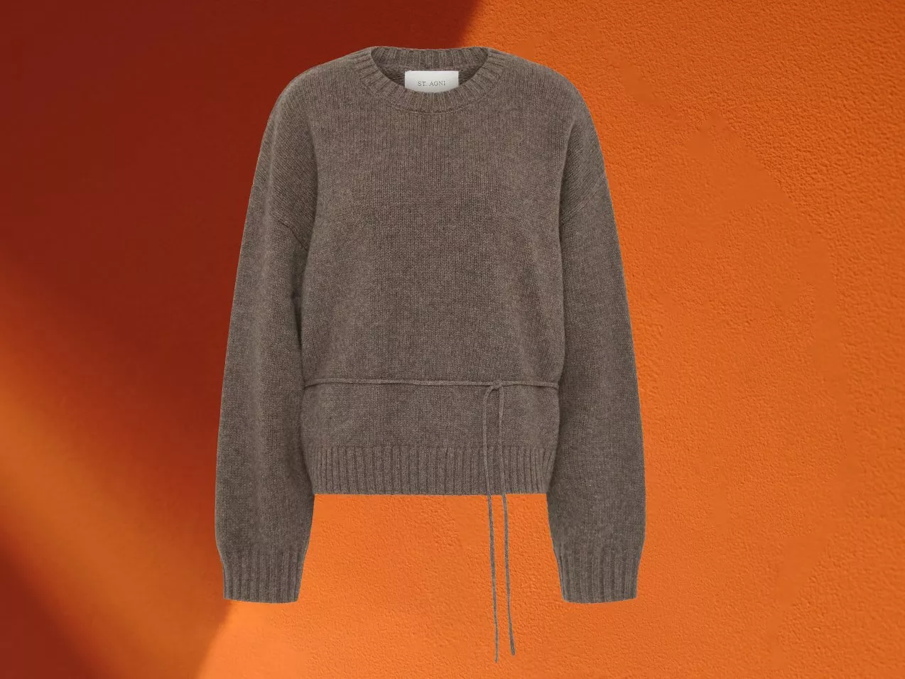 Grey knit crew neck jumper with tie waist detail, long sleeves and ribbed hem on orange background