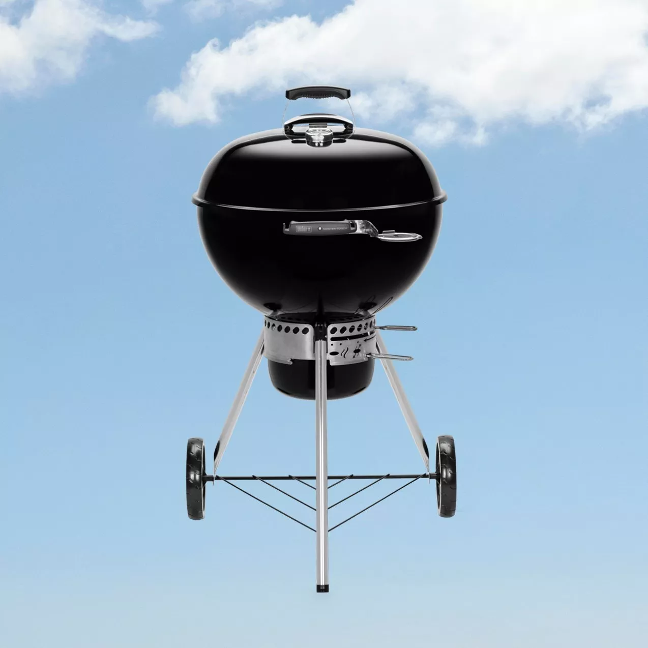 Black kettle charcoal barbecue grill on wheels, outdoor garden BBQ cooker with lid and vents under blue sky