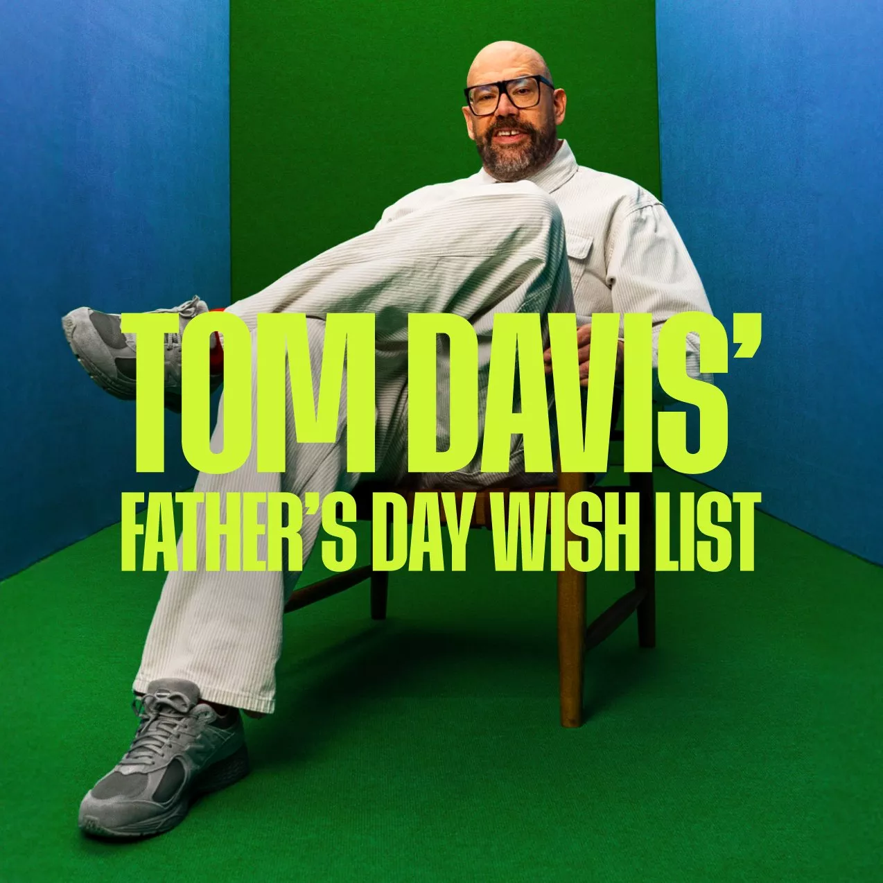 Tom Davies in white suit and trainers sitting on chair in blue and green studio room, modern portrait photo
