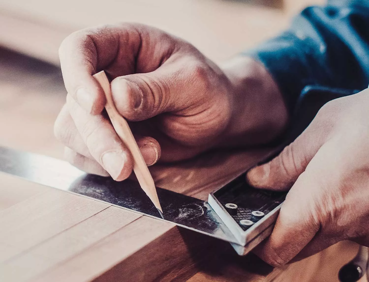 Person using a carpenter's square and a pencil to mark a line on a piece of wood