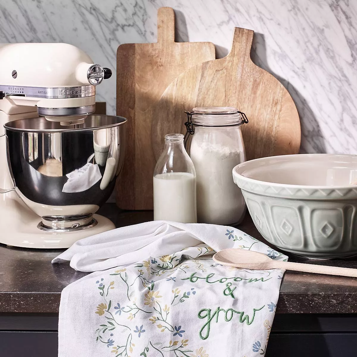 Stand mixer on a counter with a mixing bowl, wooden spoon, and floral tea towel