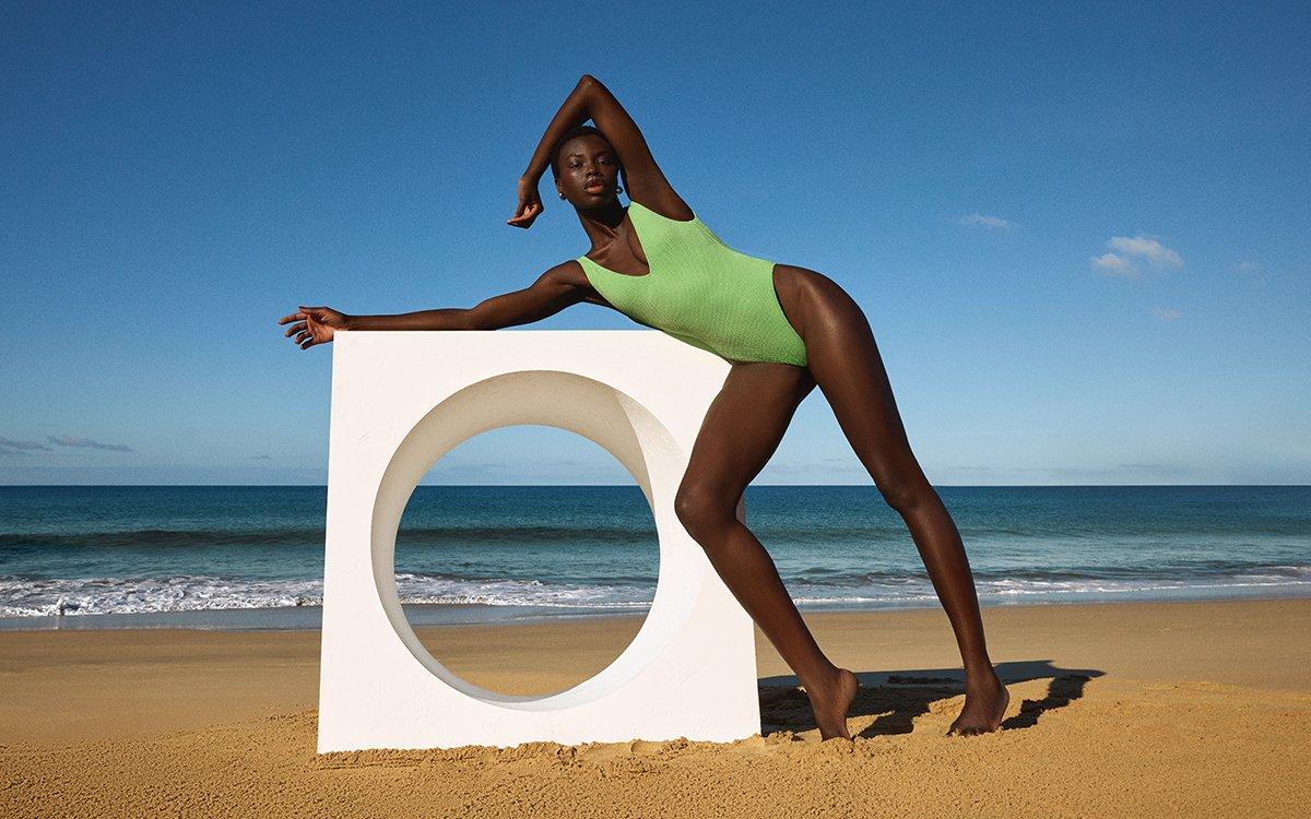 Female model on a sandy beach wearing a green high leg swimsuit