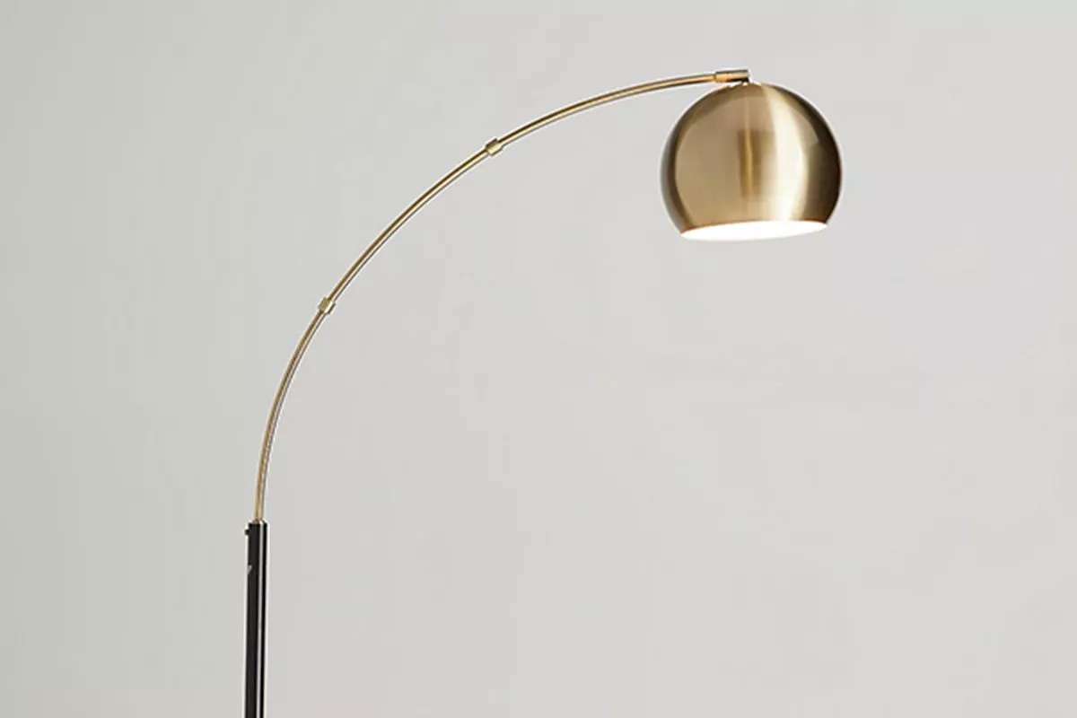 Modern brass arc floor lamp with curved arm and dome shade, minimalist lighting on neutral wall background
