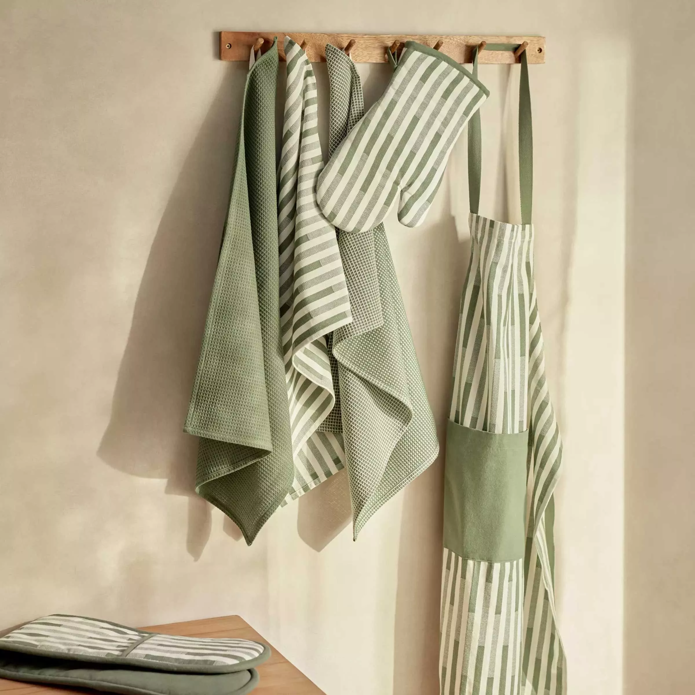 White and green stripe tea towels, oven glove and apron hung on the wall with wooden hooks