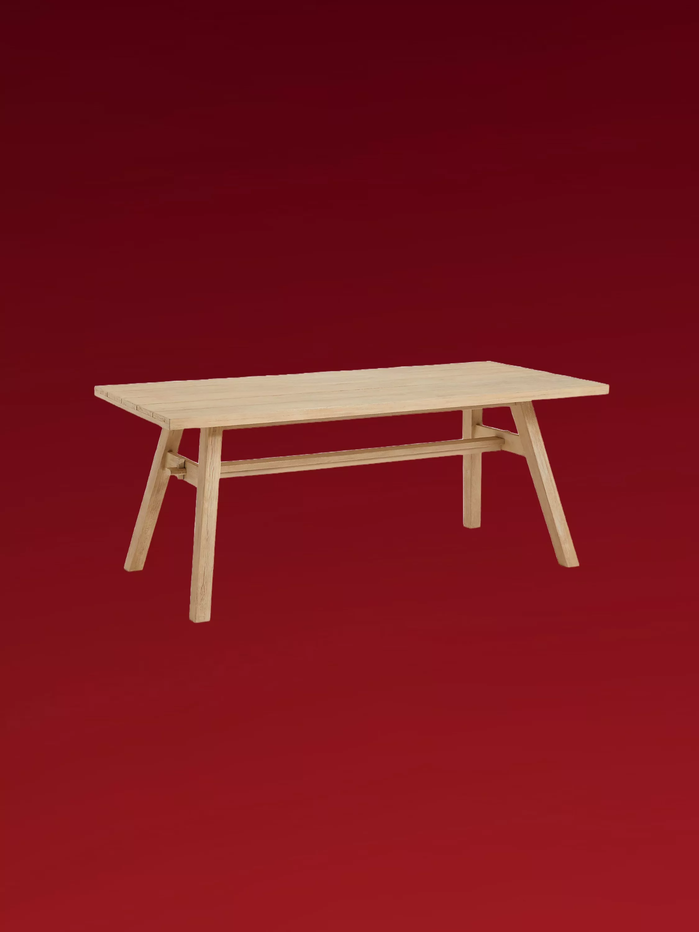 Light oak trestle dining table with angled legs and stretcher rail, photographed against a deep red background