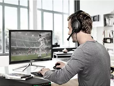 Man wearing gaming headset playing console with controller on sofa in living room, focused on online gameplay