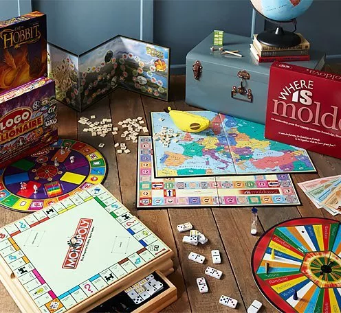 Colourful board games on wooden floor, including Monopoly and Where’s Mold? with dice, spinner and map board.