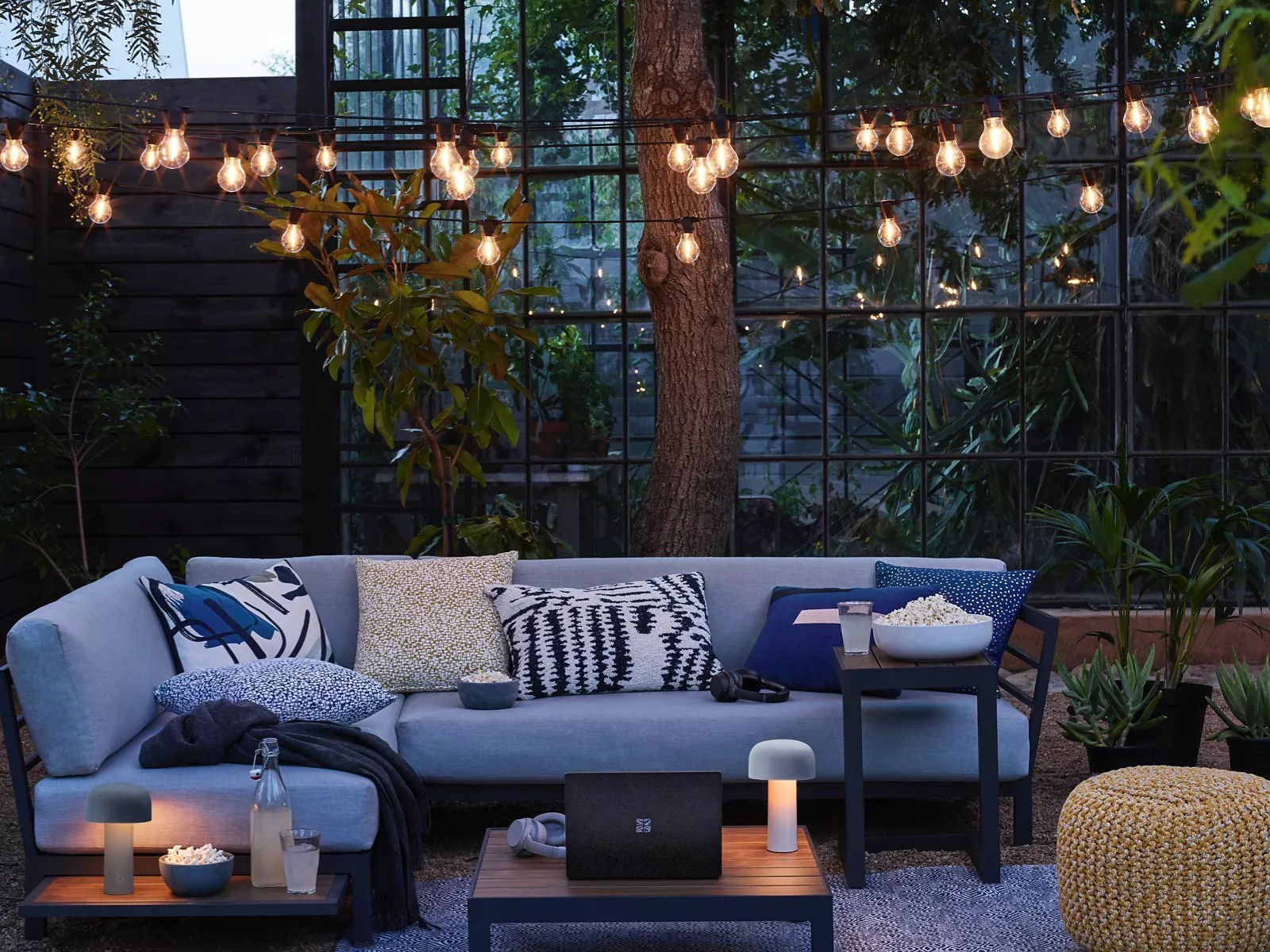 Cosy outdoor patio lounge with string lights, grey sofa, coffee table and popcorn for evening entertaining