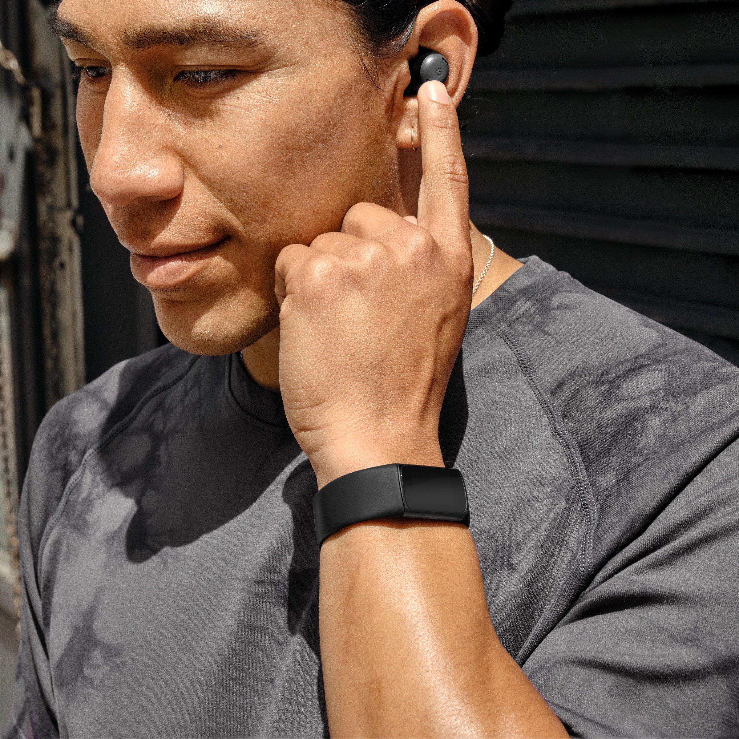Man wearing fitbit on wrist, holding finger up to his ear pressing on ear pod