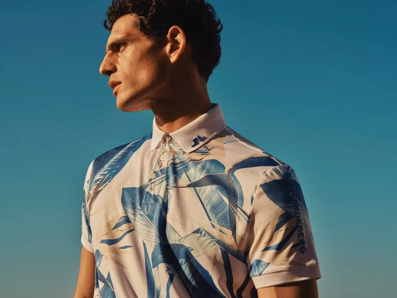 Male model in blue and white patterned polo shirt, side profile portrait against clear sky in sunlight