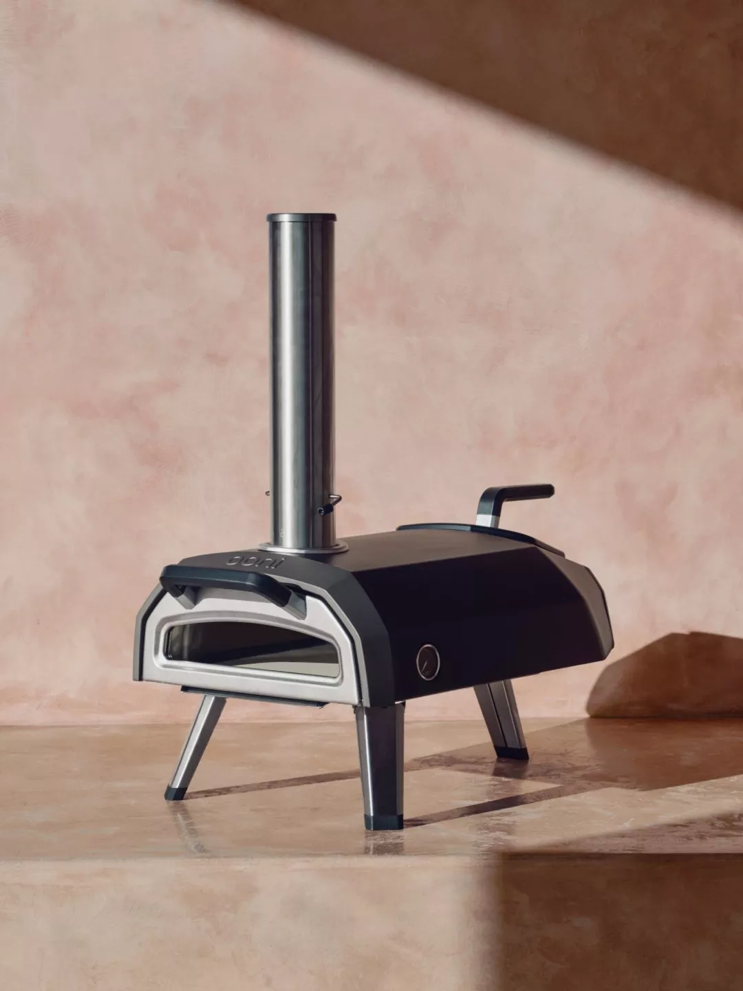 Compact outdoor wood-fired pizza oven with chimney and folding legs on a stone floor background