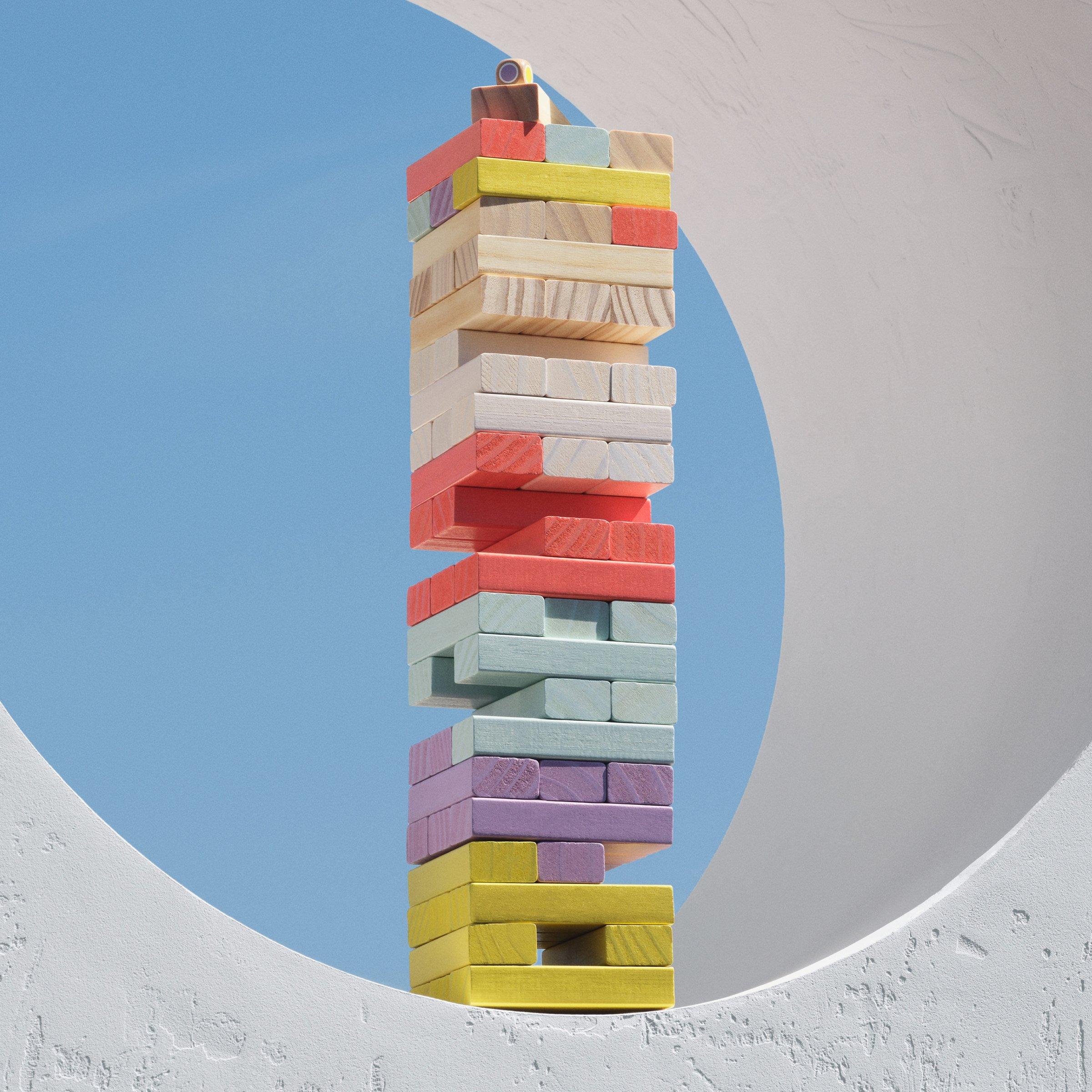 multi-coloured wooden tumbling tower game on a white wall and blue sky behind it