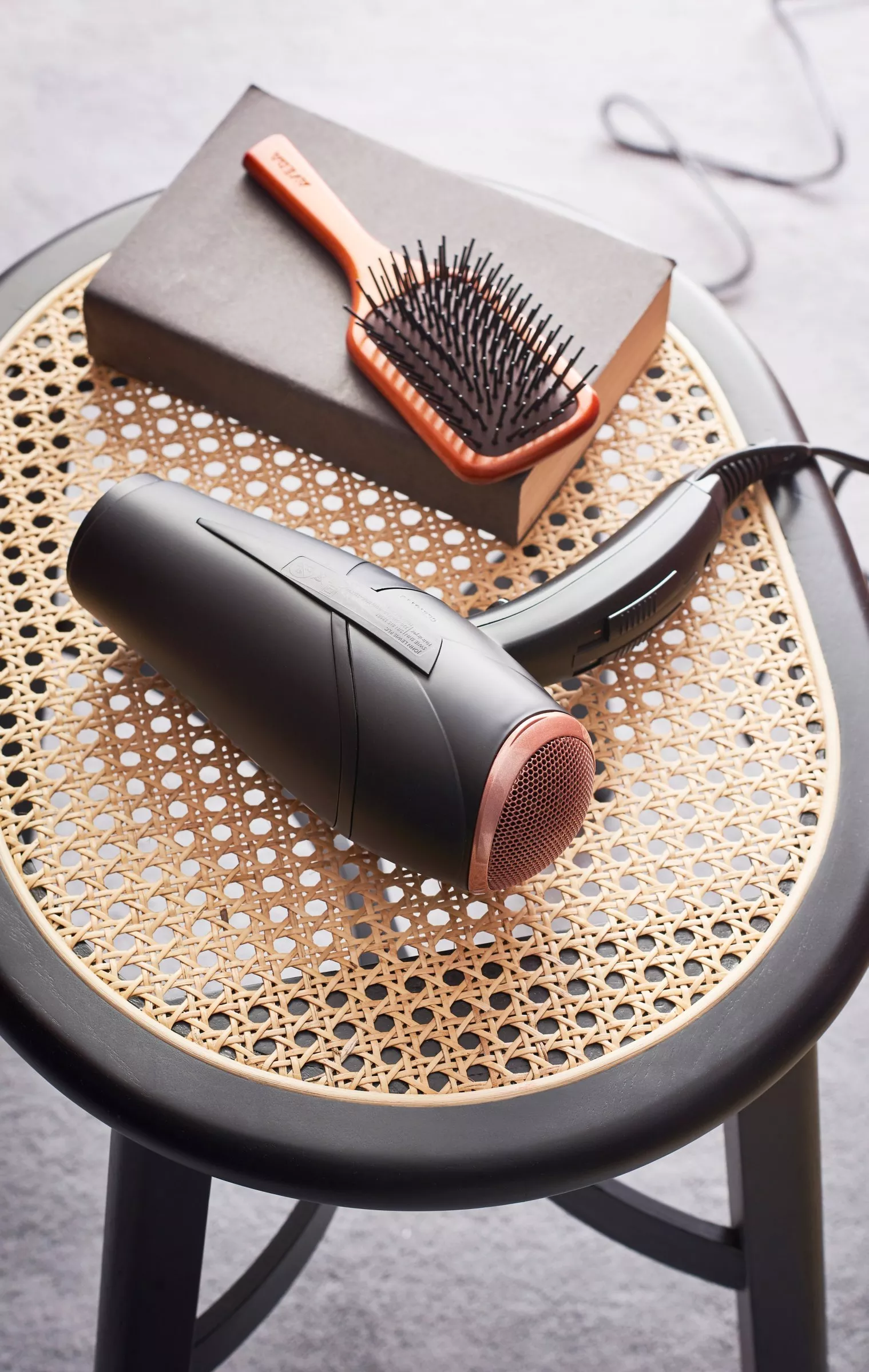 Black hair dryer and paddle brush on rattan chair seat, salon hair styling tools on tabletop background