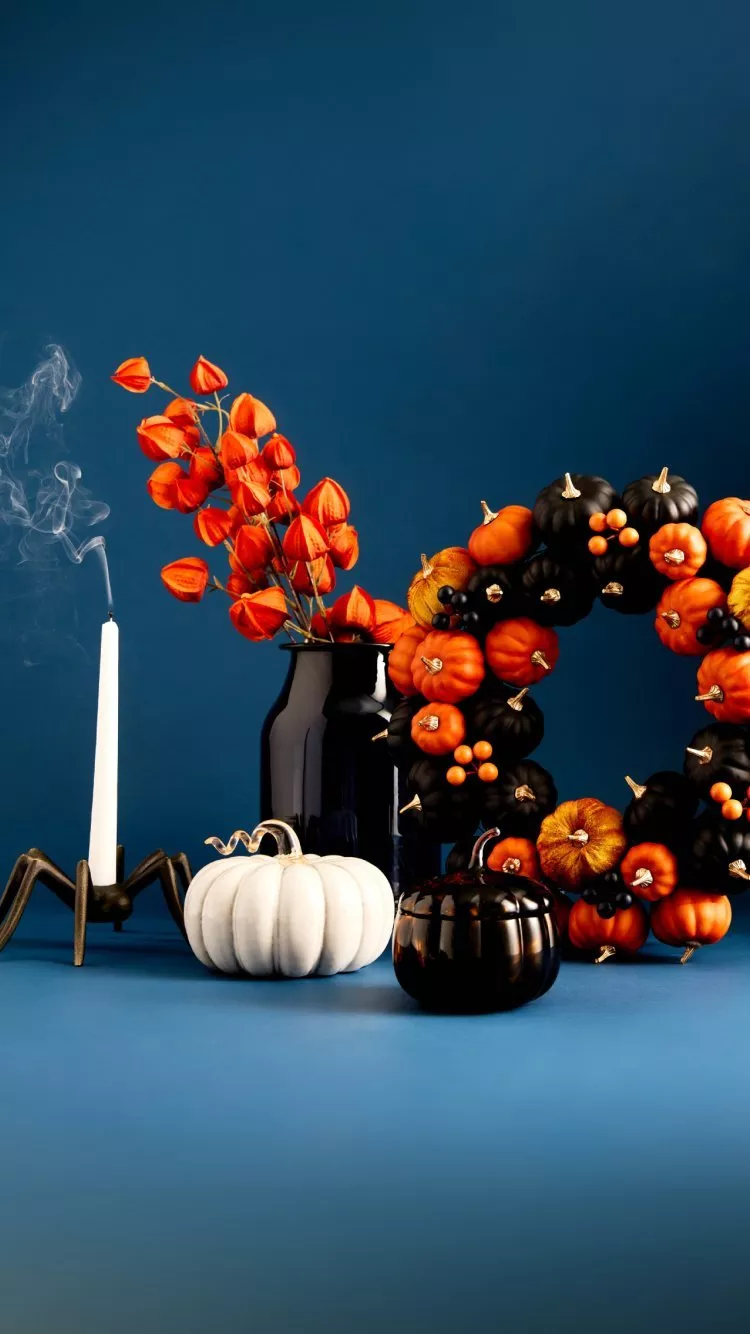 Halloween still life with pumpkins, wreath, smoking candle and orange flowers on a dark blue background